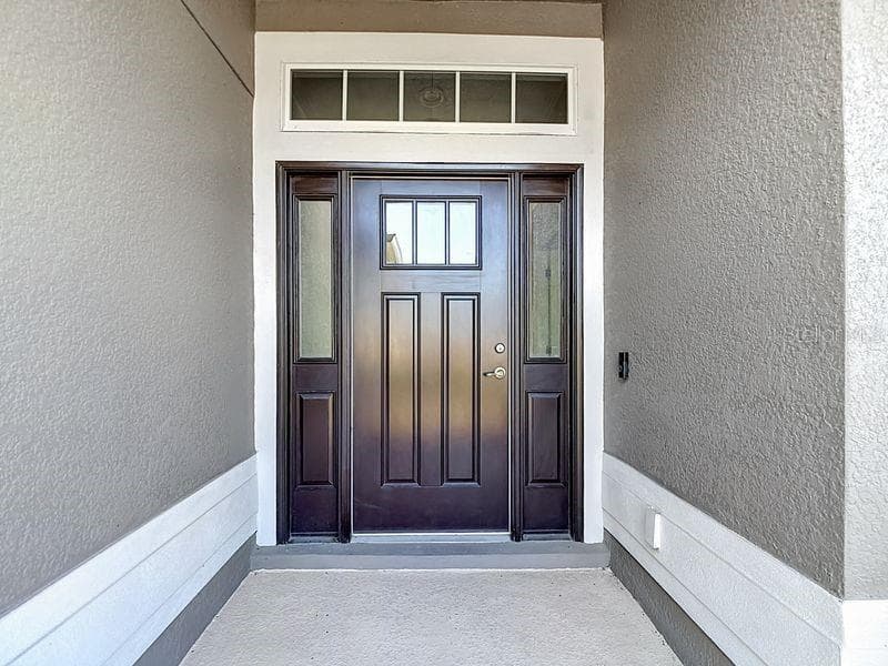 A stately front entrance featuring a rich, dark color accented by decorative glass panels and transom window that fills the space with natural light - 12244 LOOPBACK DR, SAN ANTONIO