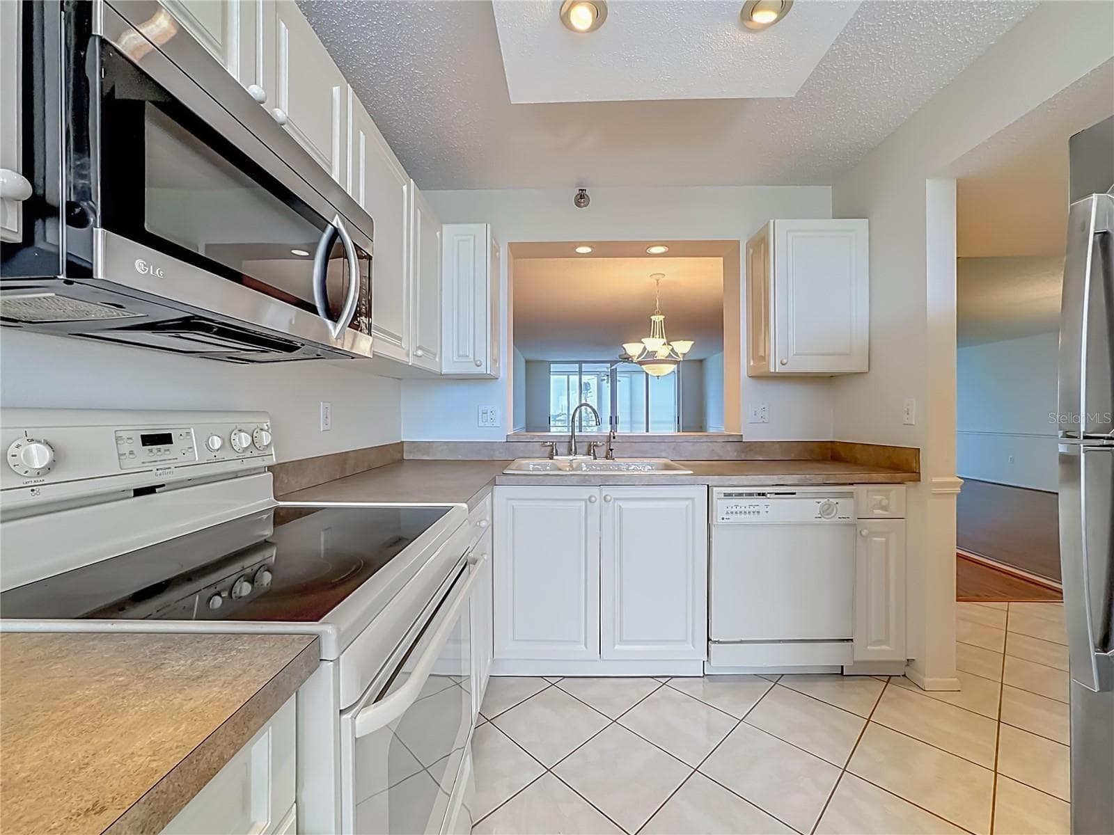Kitchen with white cabinets and stainless steel microwave and refrigerator. Pass through to the dining room. - 3740 PINEBROOK CIR #607, BRADENTON
