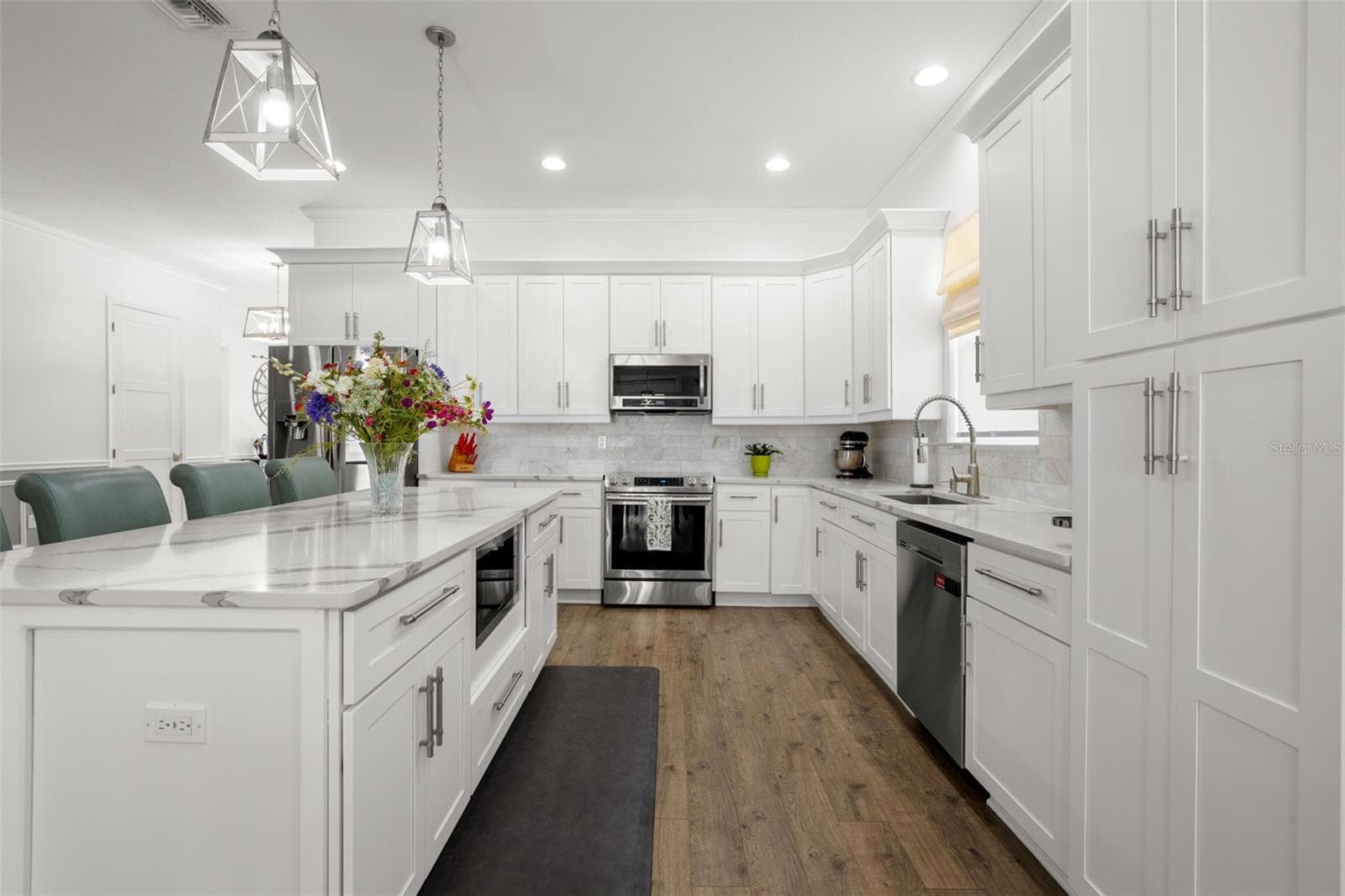The chef-inspired kitchen combines clean architectural lines with high-end finishes, including white shaker cabinetry with crown molding, designer quartz countertops, an oversized center island with additional storage and seating, upgraded stainless appliances, and an undermount farmhouse sink. An elegant onyx marble backsplash, pendant lighting, recessed lighting, and extensive cabinetry complete the beautifully designed space. - 1720 VERDE DR, CLEARWATER