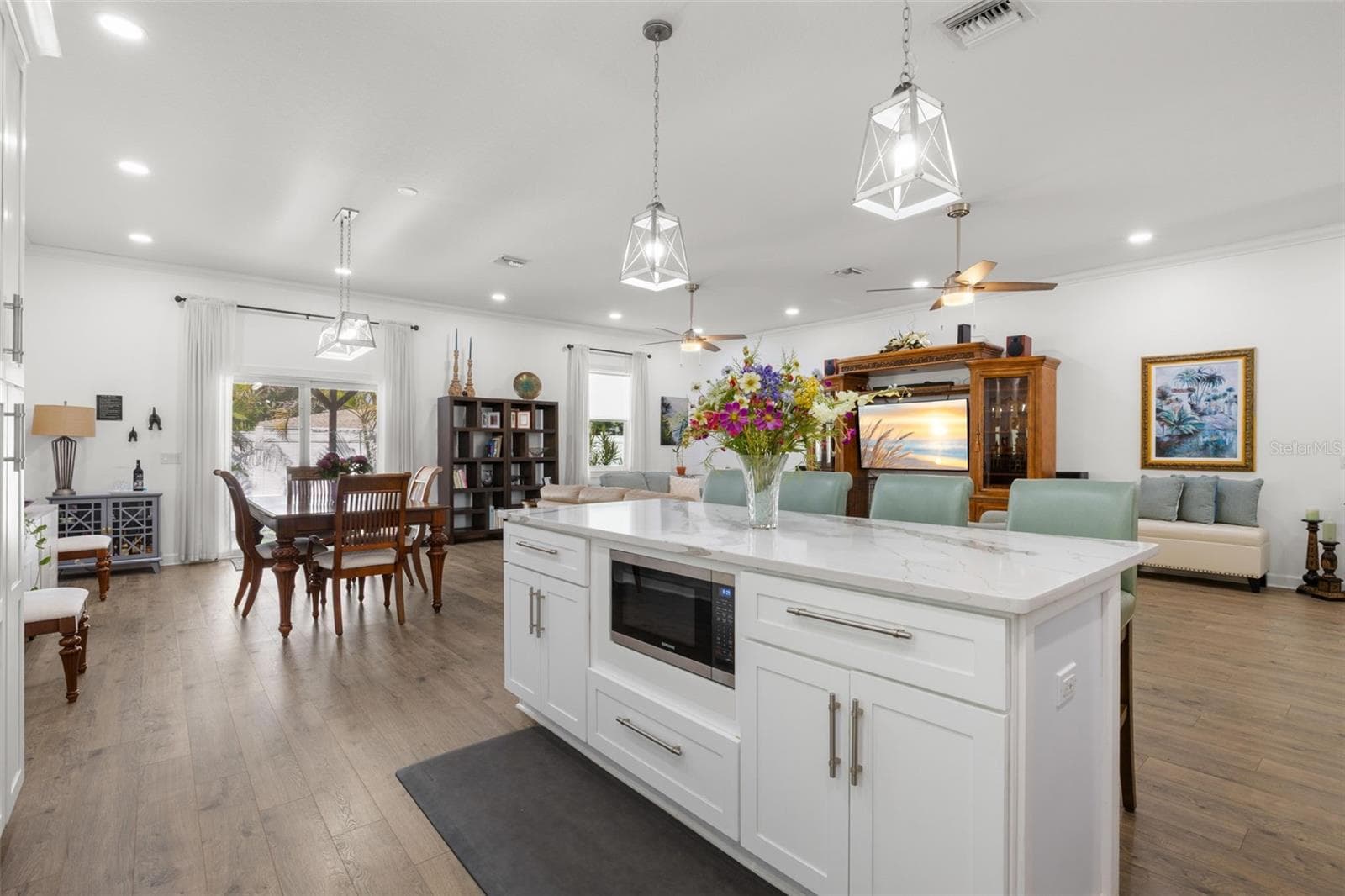 The oversized center island serves as a striking focal point within the open-concept living space, offering designer quartz countertops, additional storage, integrated 2nd microwave, pendant lighting, and generous seating. Open sightlines connect the kitchen, dining area, and great room beneath high ceilings with recessed lighting and dual contemporary ceiling fans. - 1720 VERDE DR, CLEARWATER