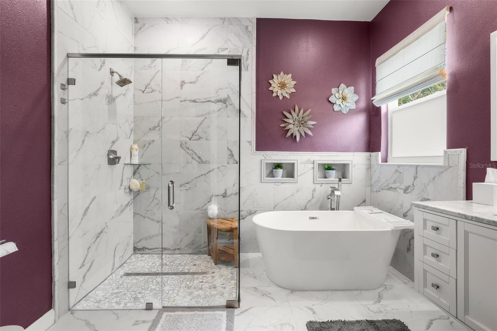 The spa-inspired primary bath showcases dramatic floor-to-ceiling designer tile, a frameless glass walk-in shower with rain shower head, freestanding soaking tub, designer quartz countertops, and upgraded plumbing fixtures. Decorative wall niches, abundant natural light, and contemporary finishes create a luxurious retreat-like atmosphere. - 1720 VERDE DR, CLEARWATER