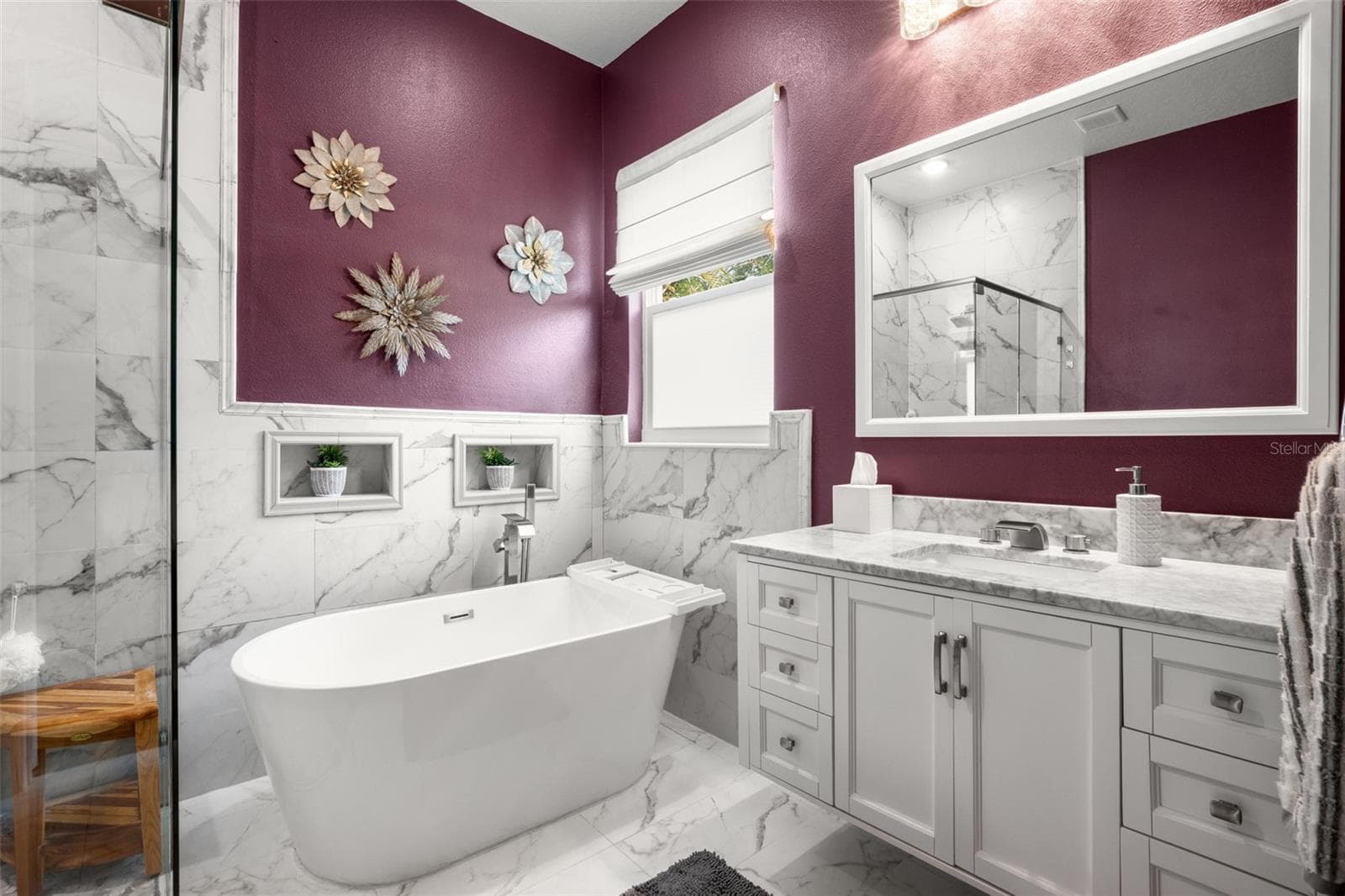 The luxurious primary bath features a freestanding soaking tub, frameless glass walk-in shower with rain shower head, designer quartz countertops, upgraded cabinetry, and dramatic marble-look tile extending throughout the space. Decorative wall niches, upgraded plumbing fixtures, and natural light enhance the spa-like atmosphere. - 1720 VERDE DR, CLEARWATER