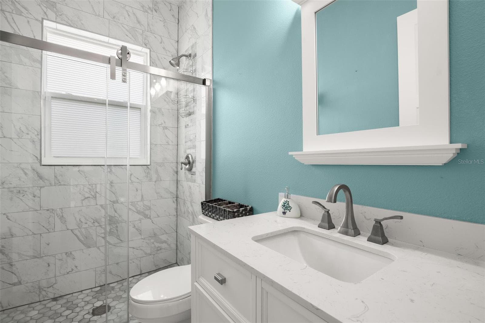Bathroom 2 features a frameless glass walk-in shower with marble-look tile, quartz countertop vanity, upgraded fixtures, and abundant natural light. - 1720 VERDE DR, CLEARWATER