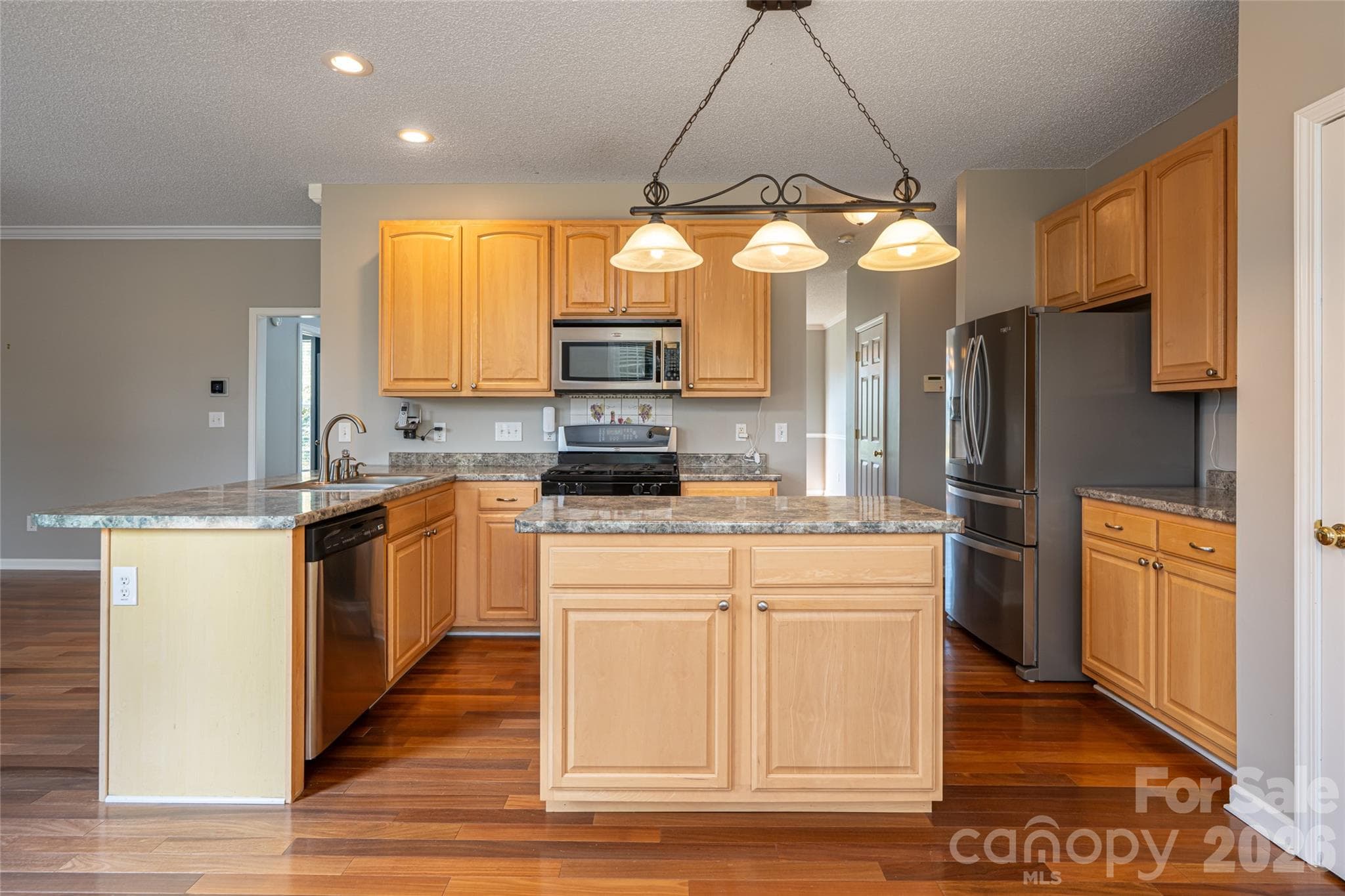 Kitchen with center island, breakfast bar, gas range, stainless appliances, pantry and pendant lighting; opens to family room and breakfast area. Natural gas, city water and sewer. - Fletcher