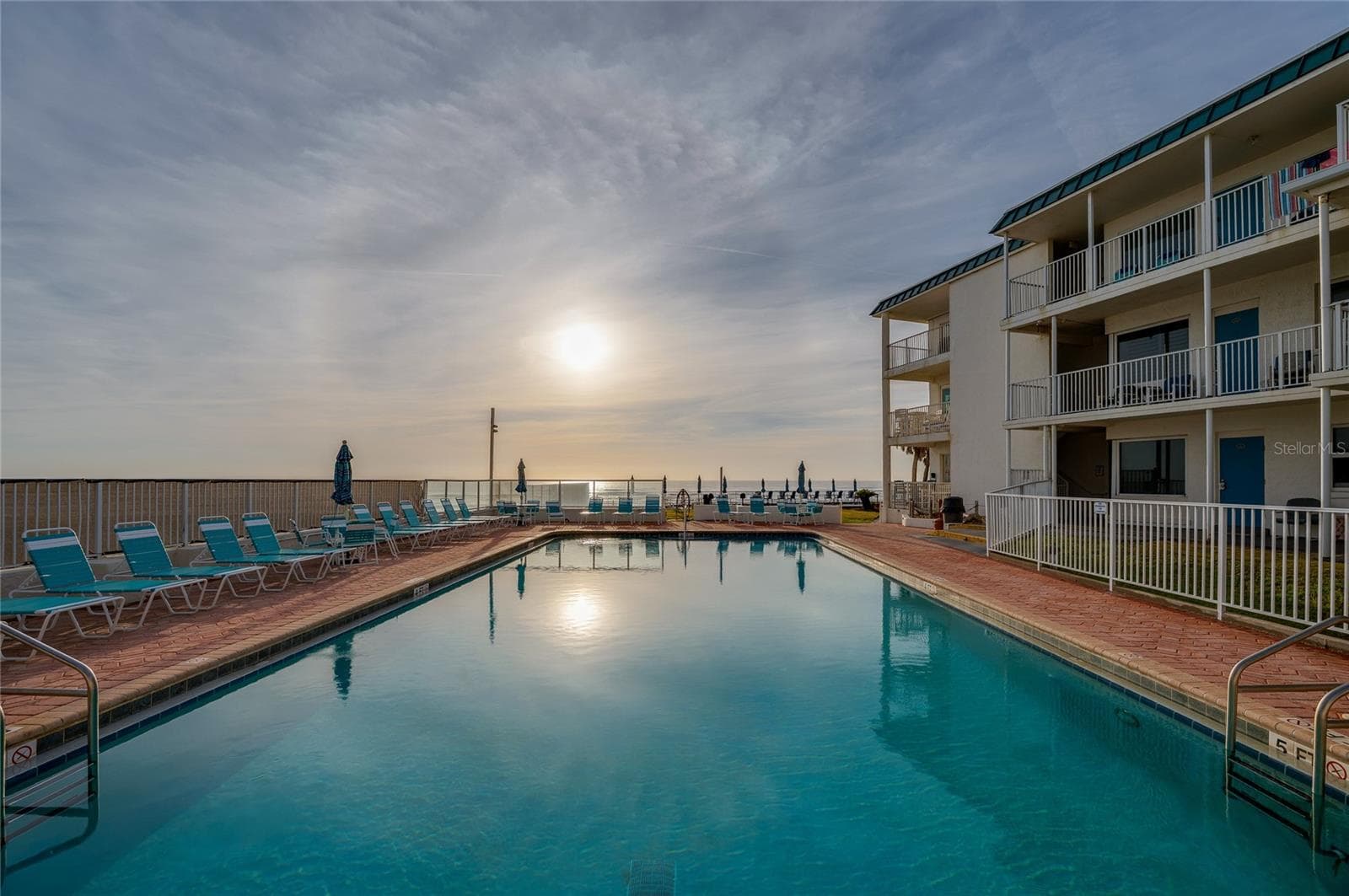 Pristine pool area featuring built-in stairs for easy entry and a dedicated lift for accessibility, all set against the backdrop of the rolling waves and blue skies. - 935 S ATLANTIC AVE #165, DAYTONA BEACH