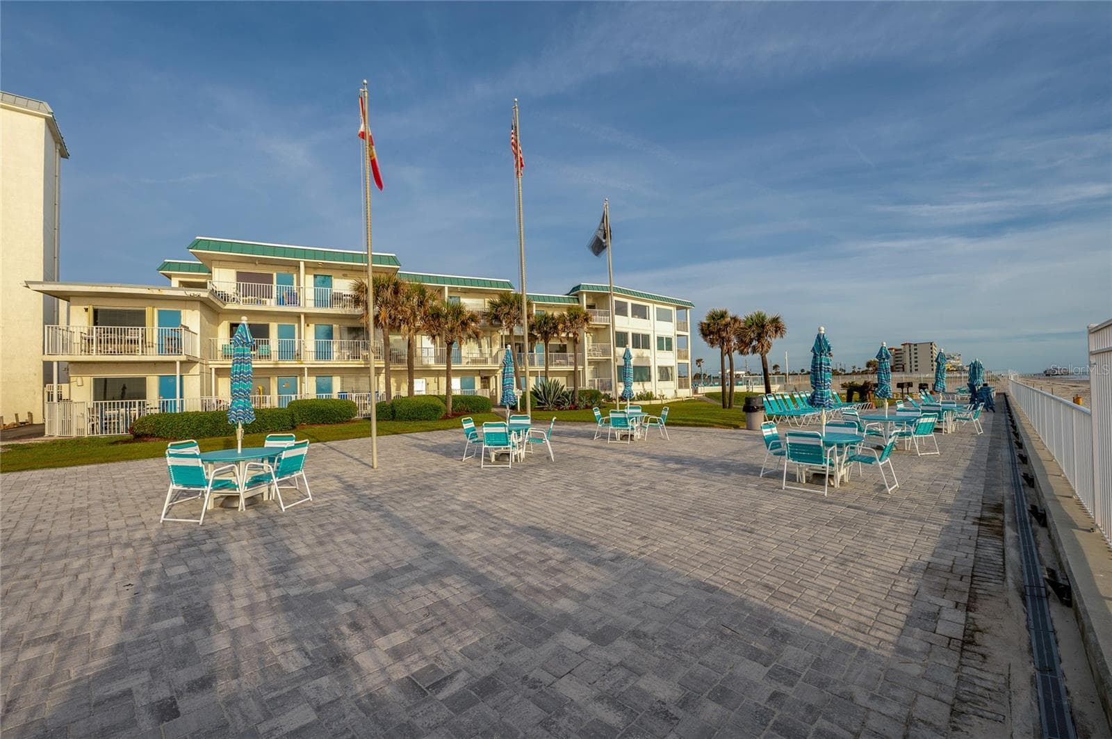 A wide-angle view of the well-maintained complex grounds, featuring extensive brick paver decking, lush palm trees, and plenty of space for sunbathing and social gatherings. - 935 S ATLANTIC AVE #165, DAYTONA BEACH