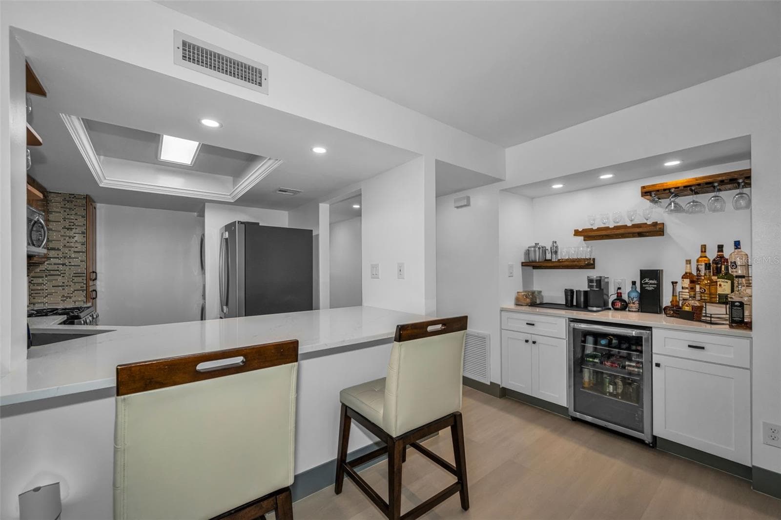 Another view of dry bar with wine refrigerator and storage cabinets, plus stools at open kitchen bar. - 5400 PARK ST N #303, ST PETERSBURG