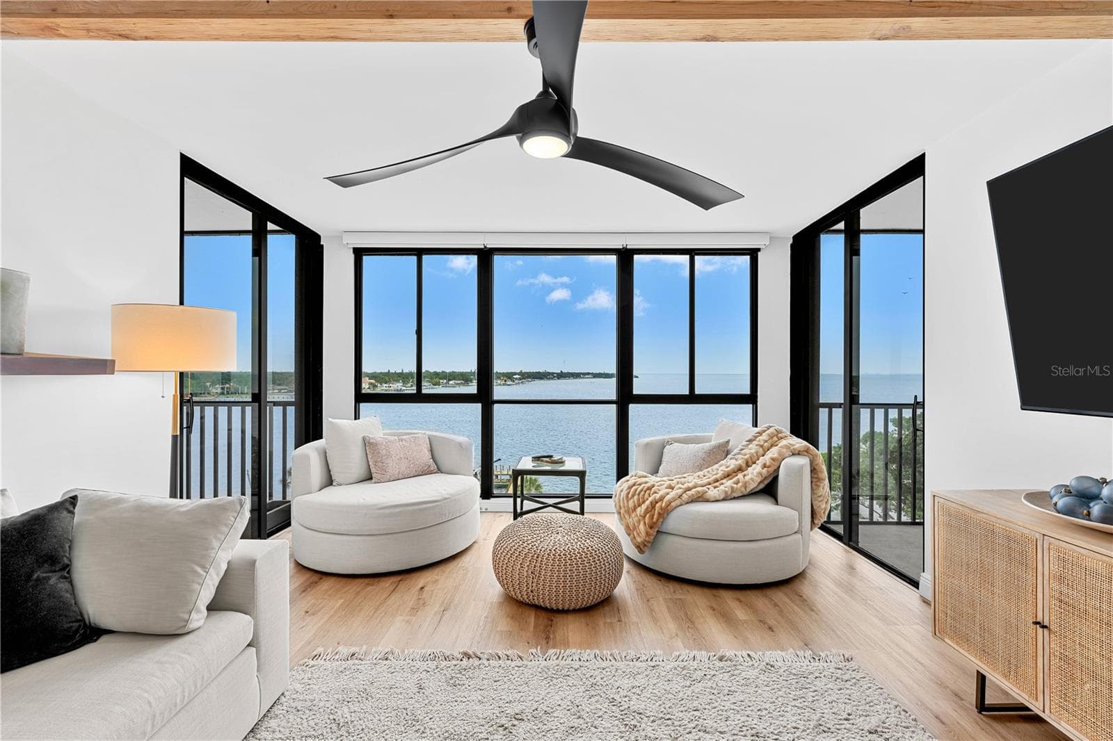 Living room with dual sliding-door balcony access, oversized swivel chairs, and wide open-water views. - 7100 SUNSHINE SKYWAY LN S #701, ST PETERSBURG