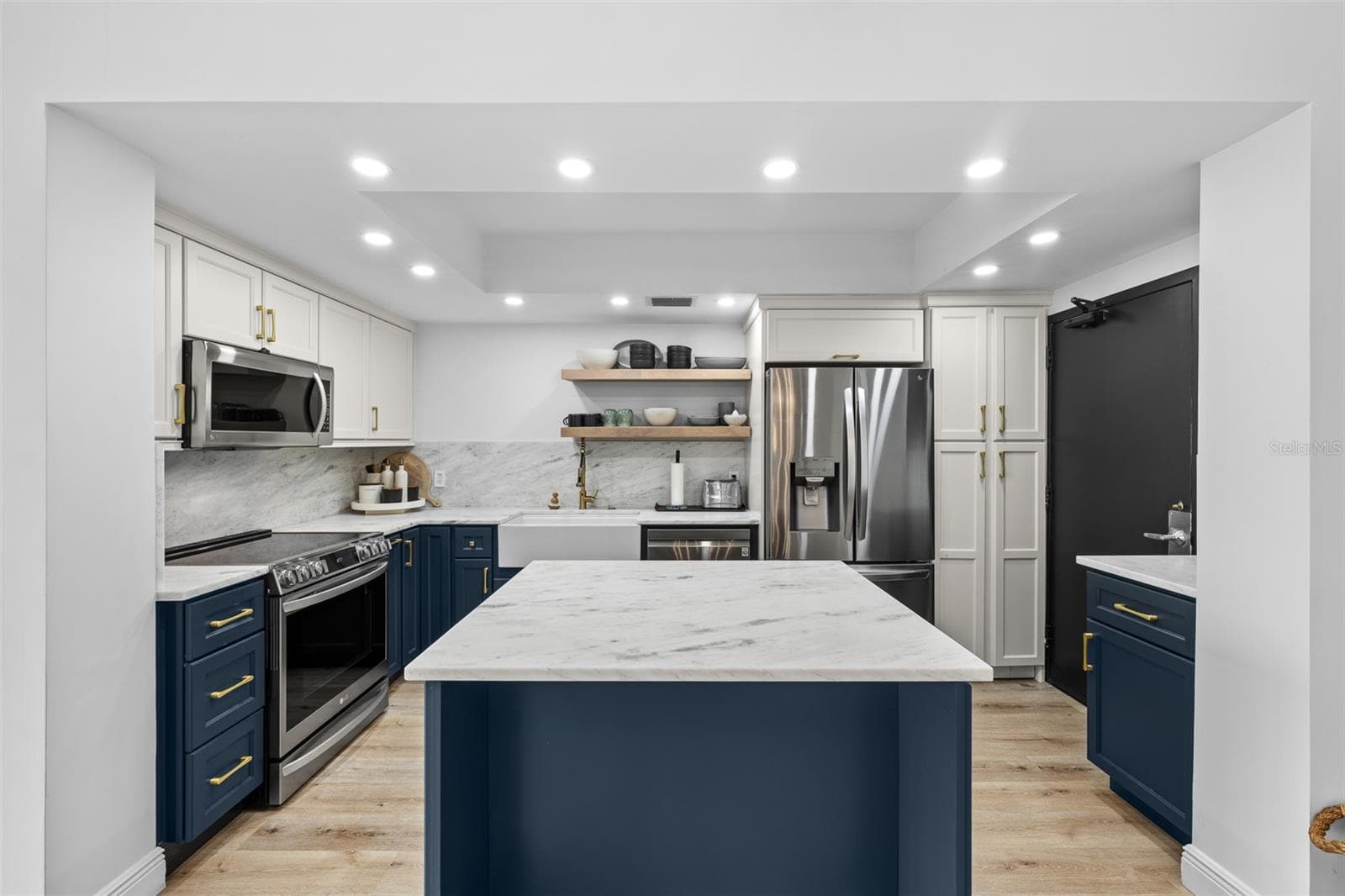 Renovated kitchen with navy shaker cabinetry, white marble counters and backsplash, farmhouse apron sink, brass hardware, and a marble-topped center island. - 7100 SUNSHINE SKYWAY LN S #701, ST PETERSBURG