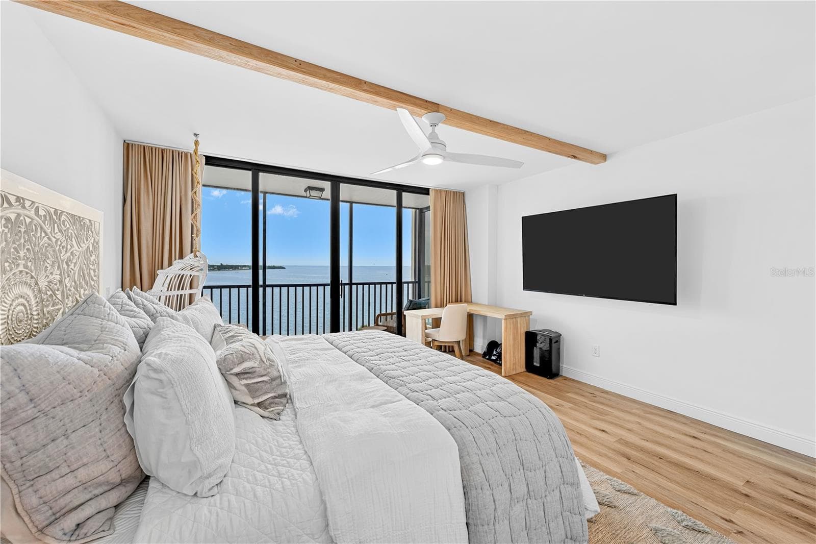 Primary bedroom with wood-beam ceiling accent, floor-to-ceiling windows, motorized blinds, and a private screened balcony framing open Tampa Bay views. - 7100 SUNSHINE SKYWAY LN S #701, ST PETERSBURG