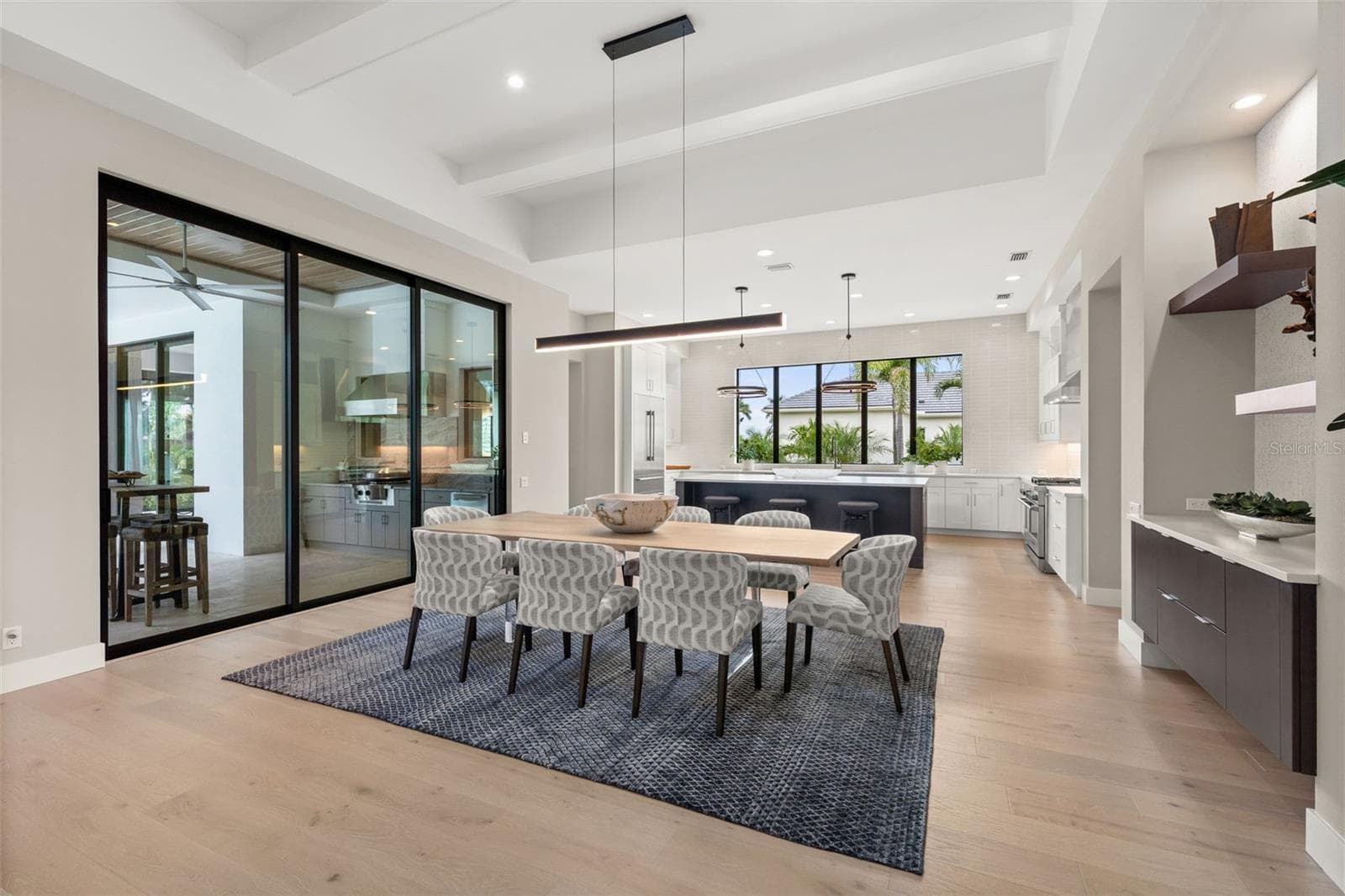 The adjacent dining room is refined, featuring a Schonbek Beyond Mystique LED linear pendant and glass sliding doors with access to the outdoor kitchen and covered lanai. - 11721 RIVE ISLE RUN, PARRISH