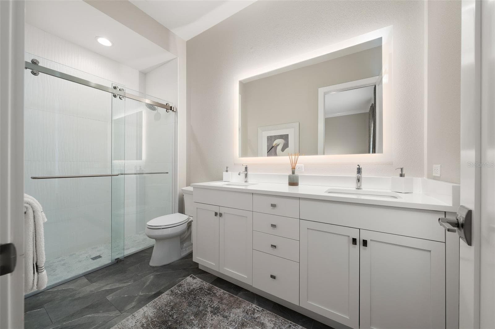 The en-suite bathroom has a double vanity, backlit mirror, porcelain tile flooring and walk-in shower with glass door. - 11721 RIVE ISLE RUN, PARRISH