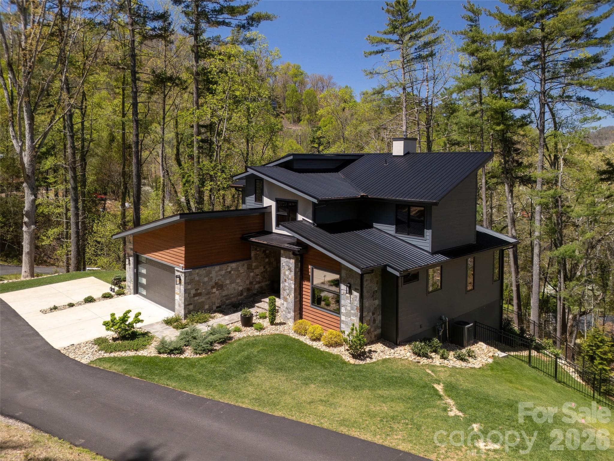 Lush mountain setting with incredible winter mountain views. You'll feel like you're living in a treehouse year-round. Beautiful roof lines, with standing seam metal roofing, highlight this mountain modern beauty. Extensive professional landcaping added since 2022. - Asheville