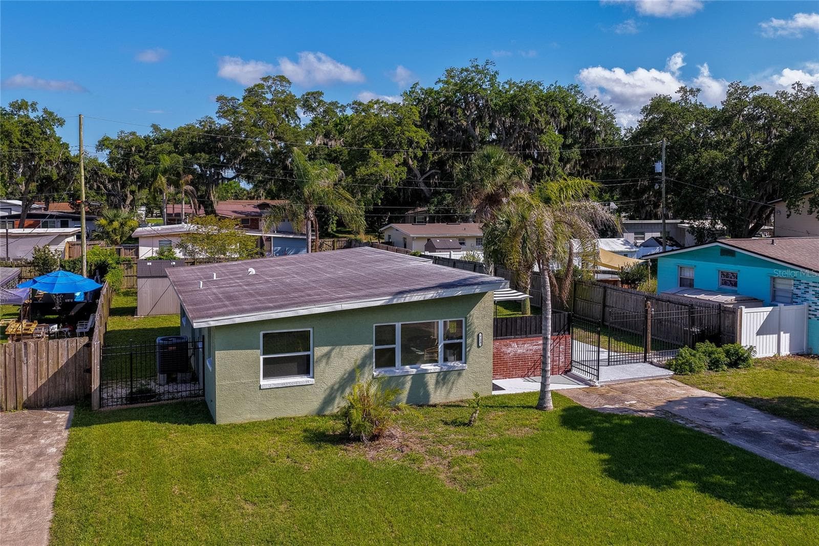 Angled street view highlighting the concrete driveway and side patio entrance of the home, framed by a mature tree in the foreground. - 723 STEELE AVE, SOUTH DAYTONA