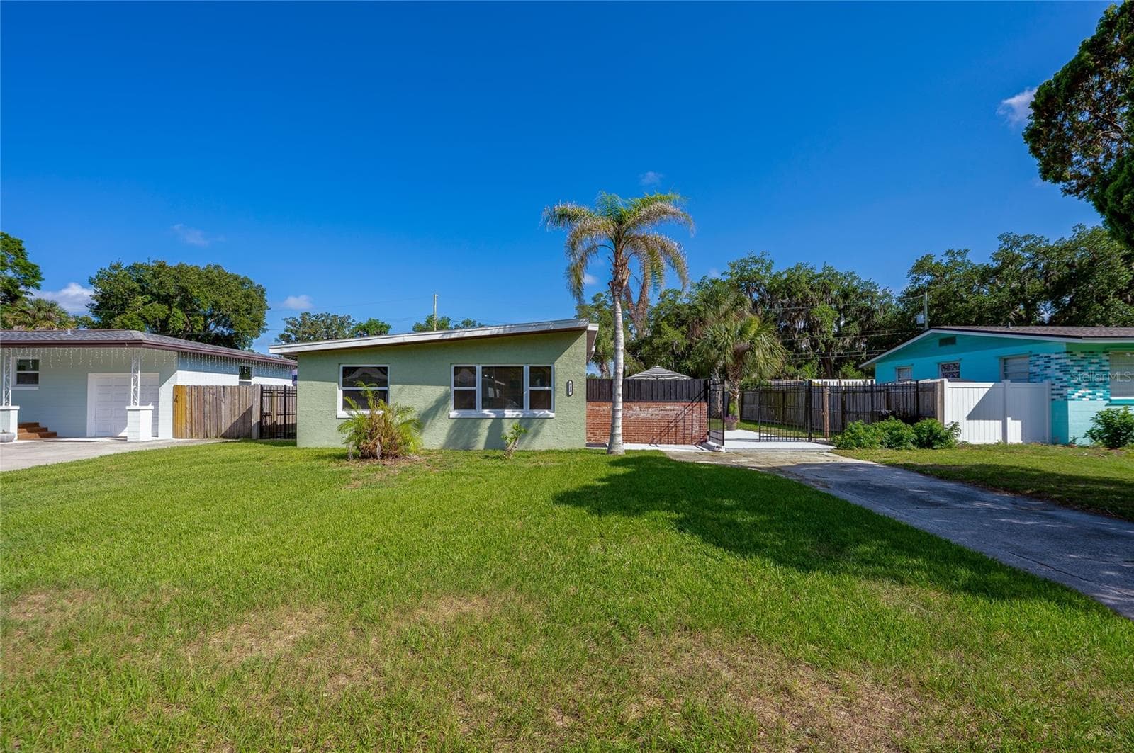 Front exterior of a charming, light green mid-century modern home showcasing a distinctive sloped roofline, a manicured lawn, and a palm tree. - 723 STEELE AVE, SOUTH DAYTONA