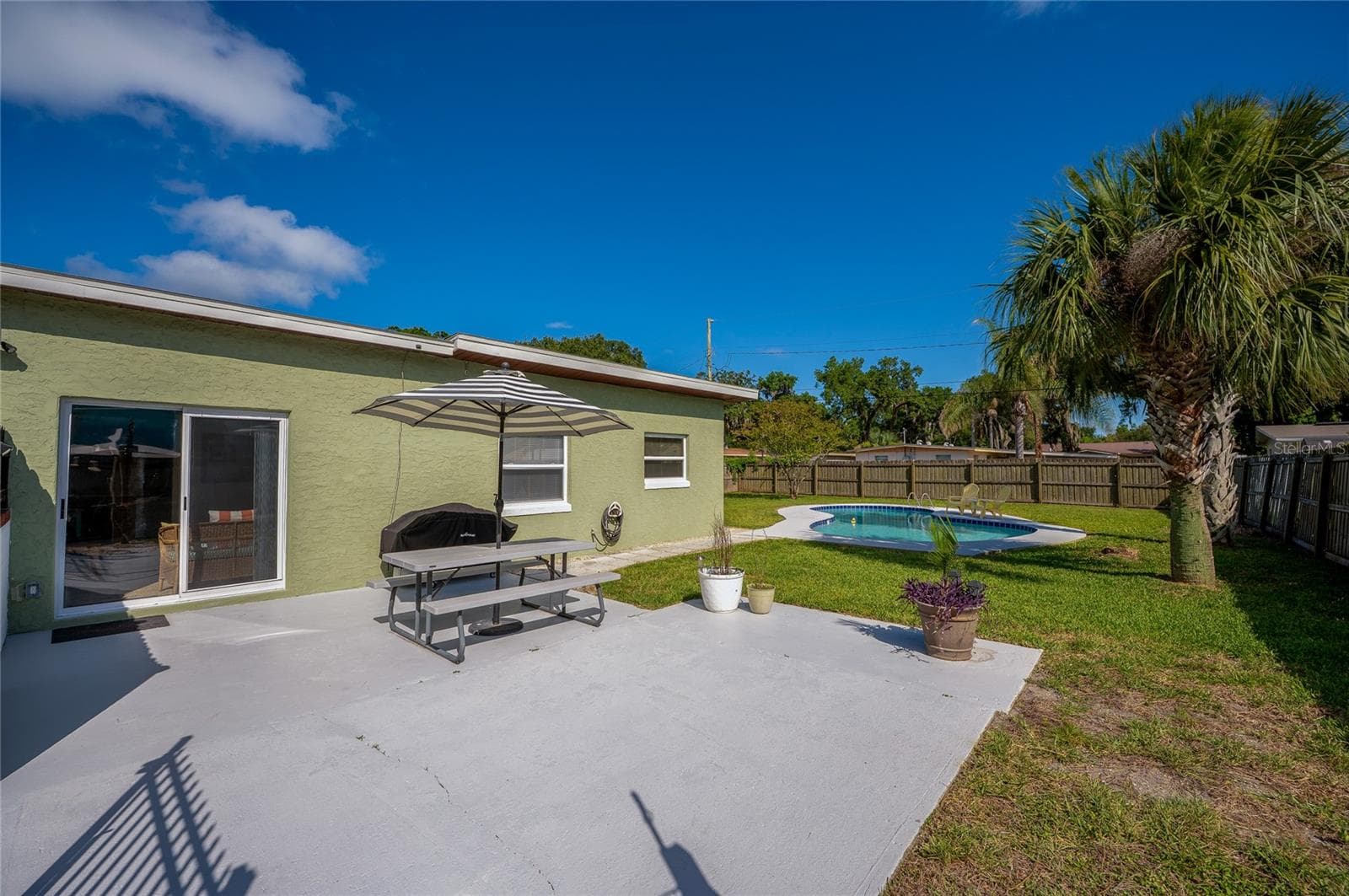 Inviting concrete patio area perfect for outdoor dining, overlooking a spacious green lawn and a private, sparkling in-ground pool. - 723 STEELE AVE, SOUTH DAYTONA