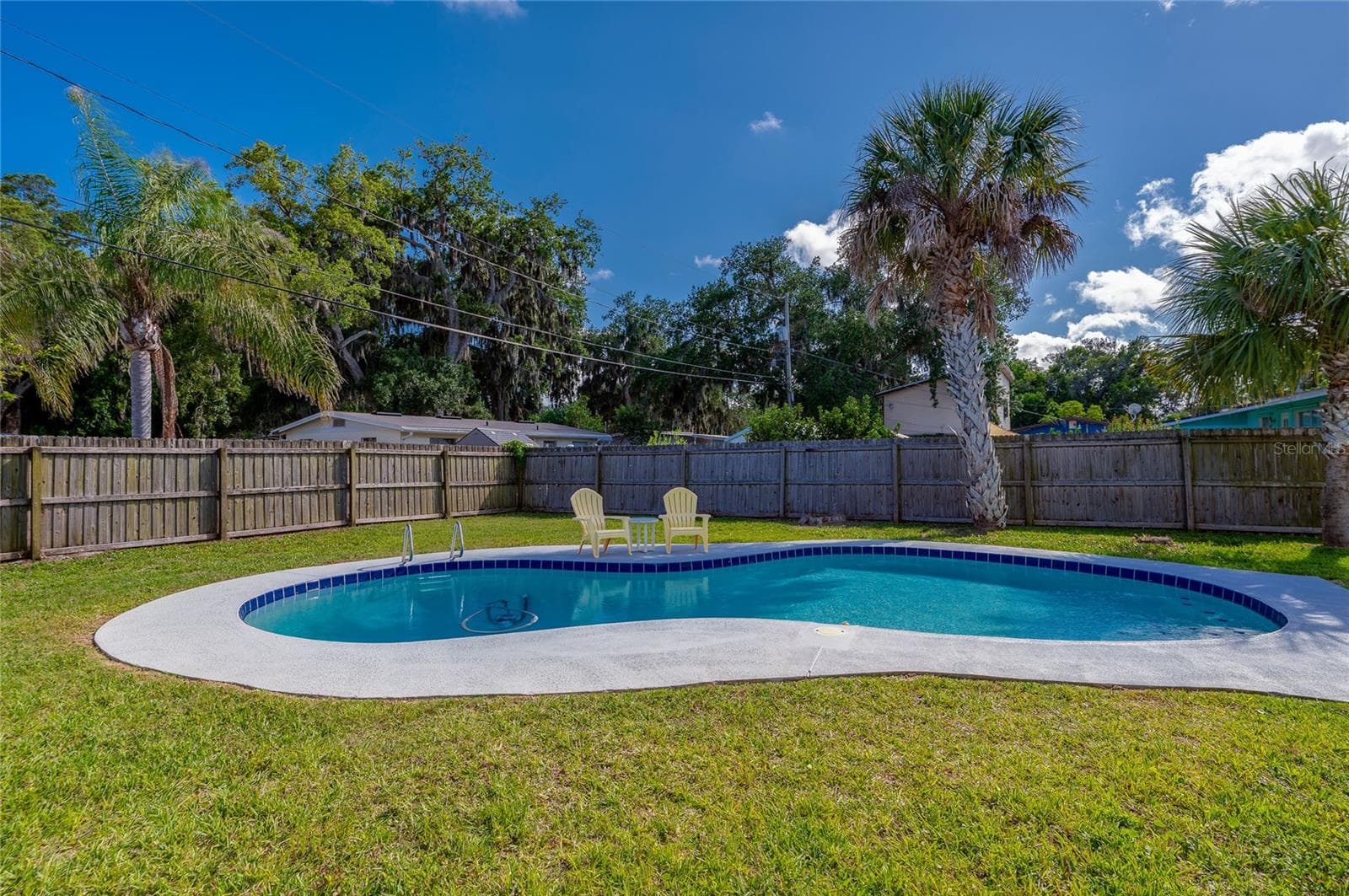 Serene poolside setting framed by a tall wooden privacy fence and a backdrop of lush, tropical foliage. - 723 STEELE AVE, SOUTH DAYTONA