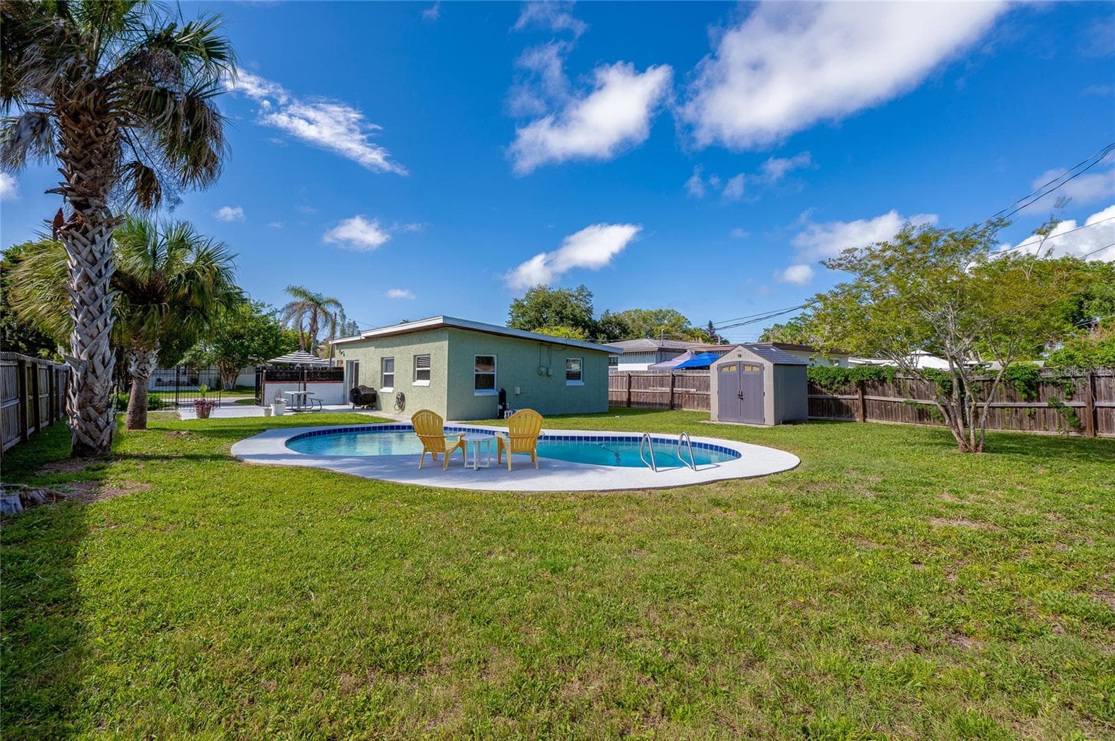 Generous backyard view showcasing the home's green exterior, a detached storage shed, and a poolside seating area. - 723 STEELE AVE, SOUTH DAYTONA