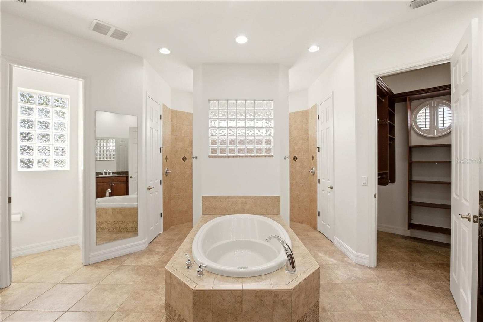 The primary bathroom features a soaking tub, split vanities with dedicated makeup counter space, a spacious walk-in shower with dual shower heads, a private water closet, and dual walk-in closets with custom organization. - 8417 LONE EAGLE WAY, SARASOTA