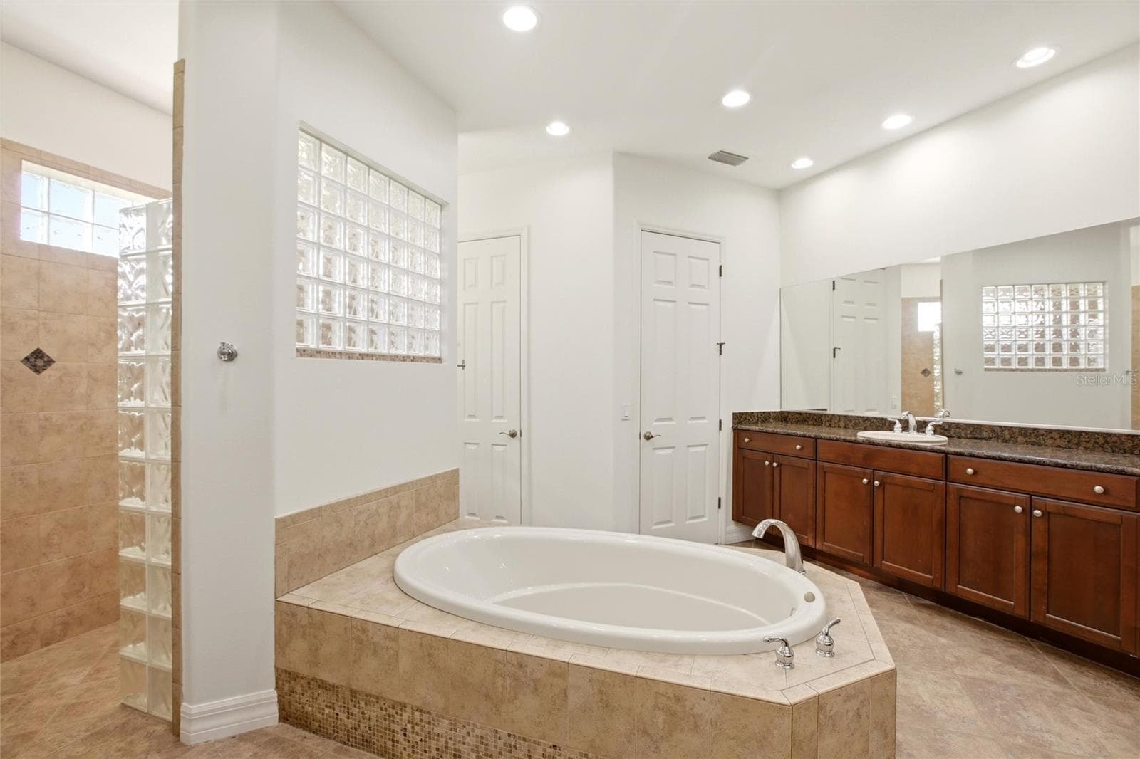 The primary bathroom features a soaking tub, split vanities with dedicated makeup counter space, a spacious walk-in shower with dual shower heads, a private water closet, and dual walk-in closets with custom organization. - 8417 LONE EAGLE WAY, SARASOTA