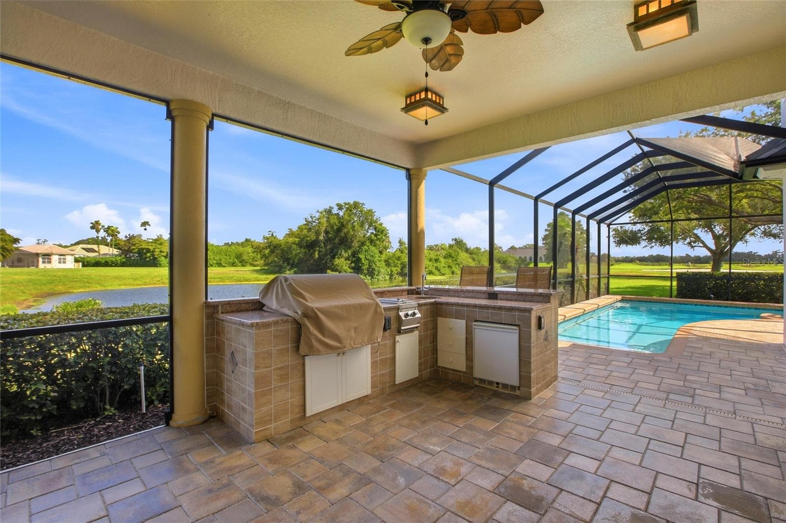 Enjoy resort-style living with a heated pool and spa, plus an outdoor kitchen complete with a gas grill, cooktop, and refrigerator — all set against picturesque golf course and water views with the peaceful backdrop of Misty Creek’s natural beauty and visiting deer. - 8417 LONE EAGLE WAY, SARASOTA