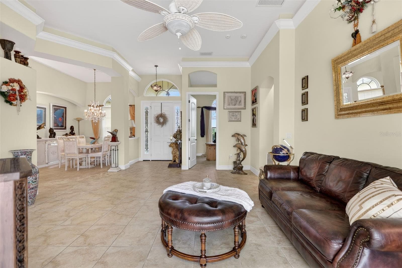Expansive formal living room showcasing double tray ceilings, crown molding, tile flooring throughout, and an open layout designed for both entertaining and everyday living. - 1210 408TH CT E, MYAKKA CITY