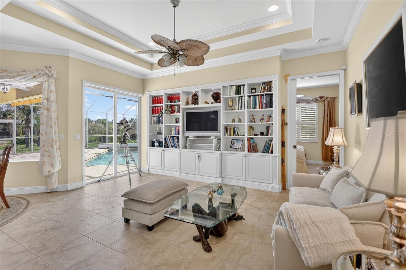 The inviting family room features a custom built-in entertainment center, tray ceiling, and seamless access to the outdoor living spaces. - 1210 408TH CT E, MYAKKA CITY