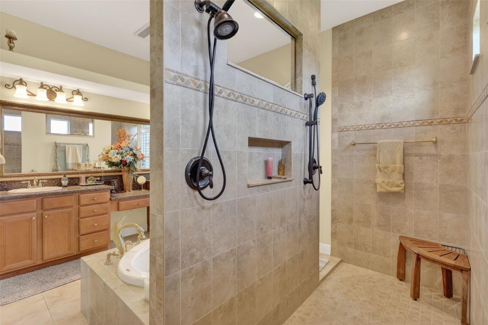 The luxurious primary bath showcases a walk-through tiled shower with dual shower heads, built-in niches, and a spacious spa-like design. - 1210 408TH CT E, MYAKKA CITY