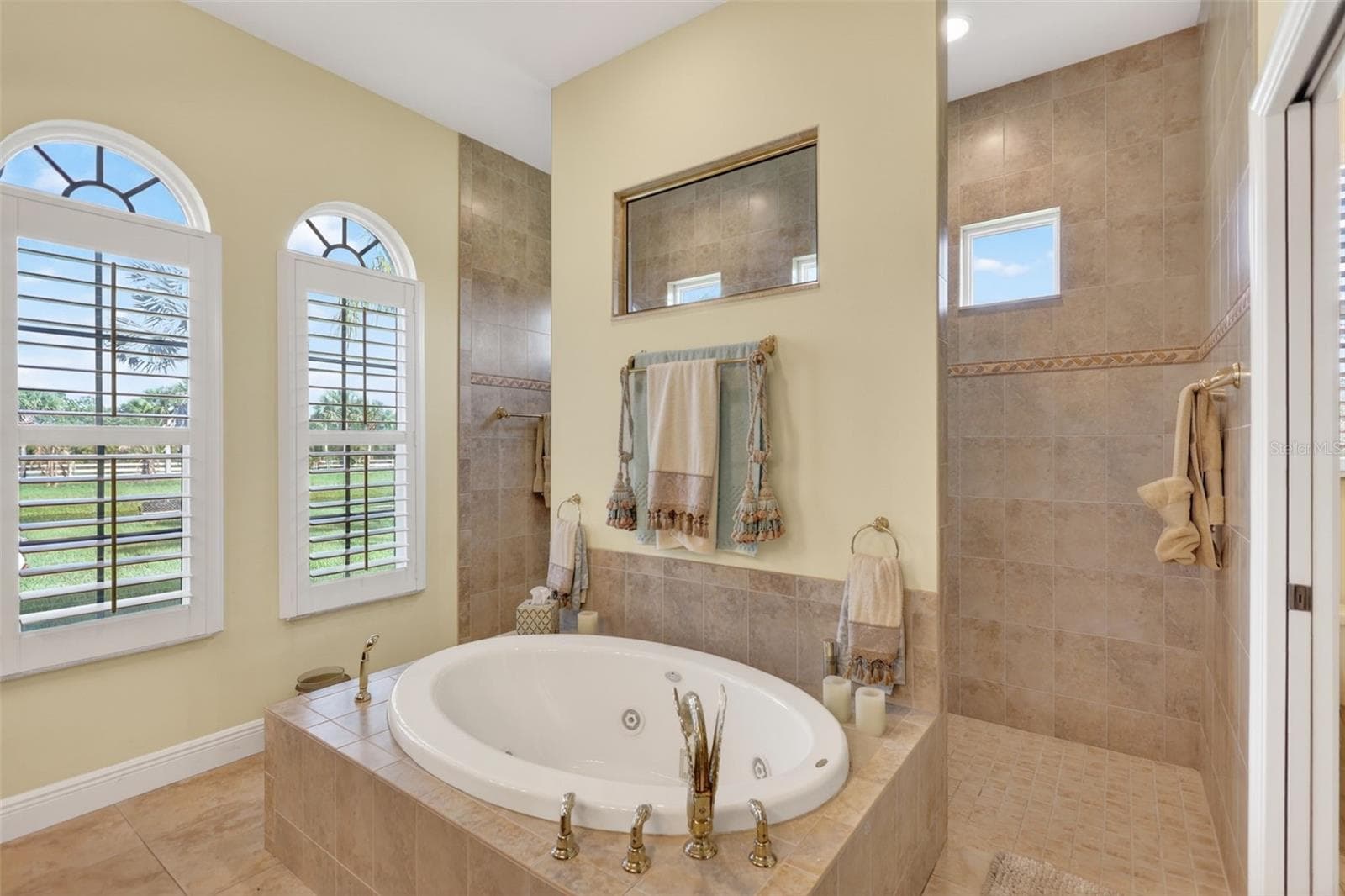 Designed with relaxation in mind, the spa-inspired primary bath offers a soaking tub, expansive walk-through shower, and peaceful views of the surrounding property. - 1210 408TH CT E, MYAKKA CITY