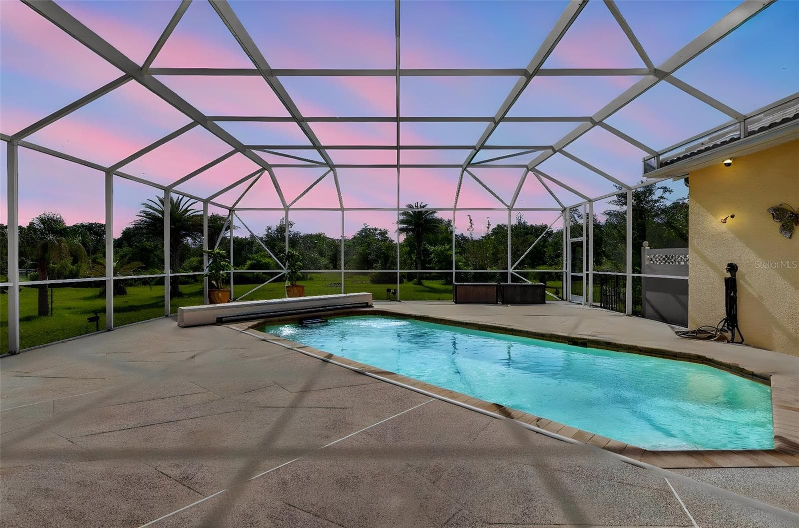 As the sun sets, the pool enclosure transforms into a serene private oasis, showcasing stunning evening skies and tranquil outdoor living. - 1210 408TH CT E, MYAKKA CITY
