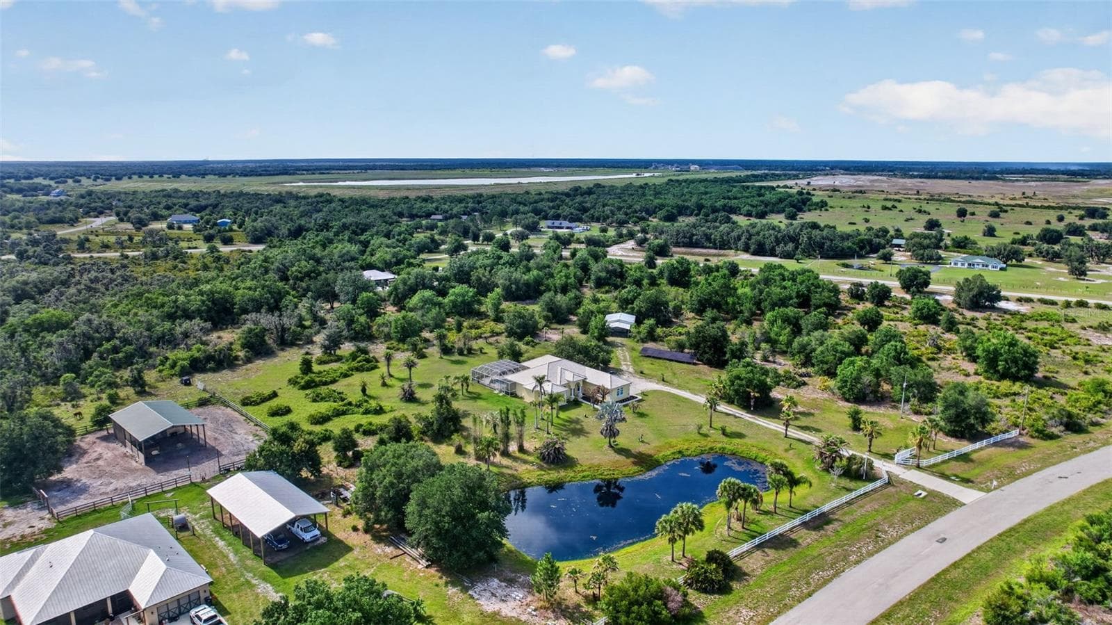 An expansive aerial view showcases the full scope of the estate, highlighting the private pond, mature landscaping, and over six acres of peaceful countryside. - 1210 408TH CT E, MYAKKA CITY