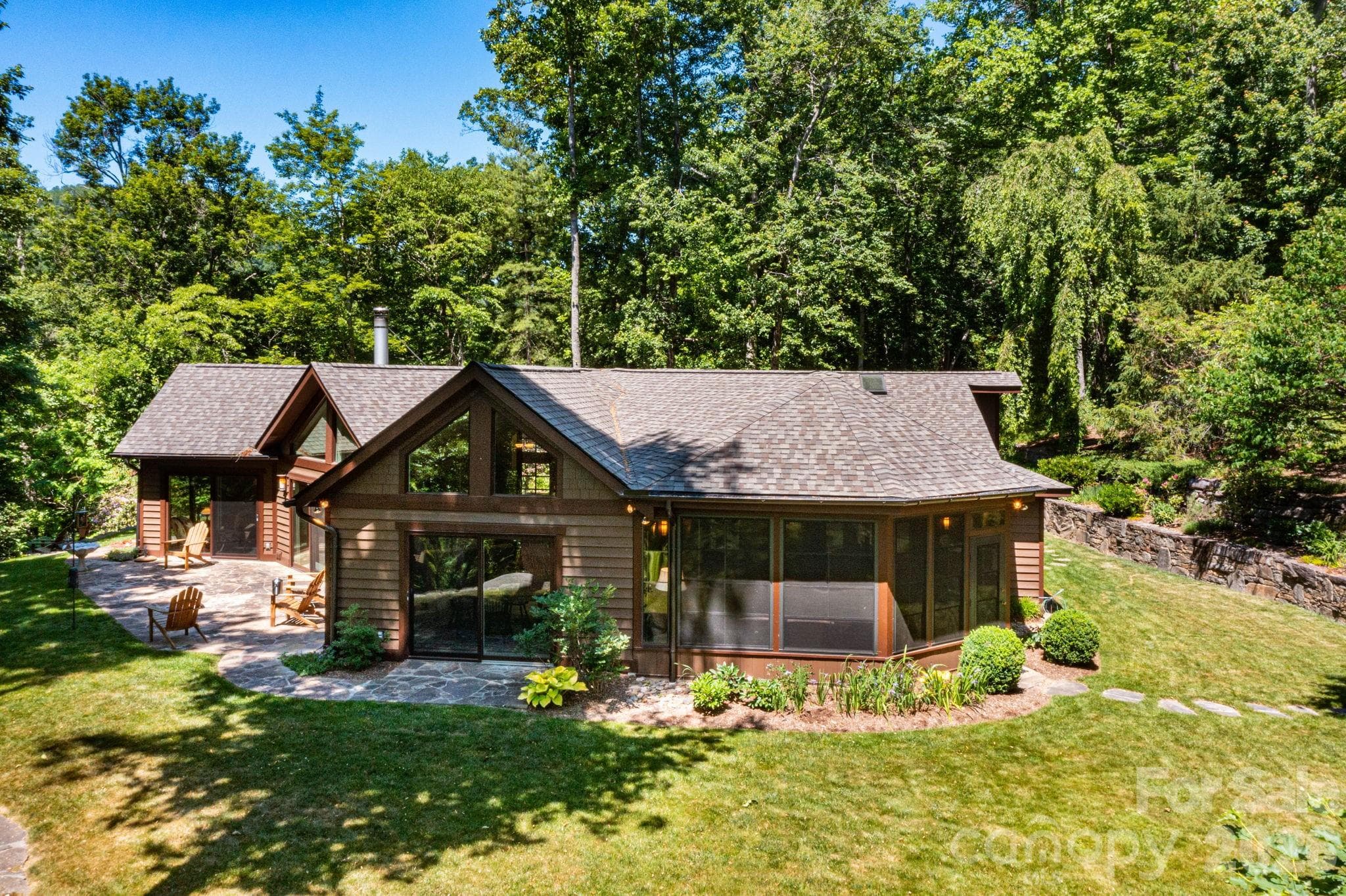 Architecturally striking mountain retreat designed to blend seamlessly with its natural surroundings. Expansive windows, soaring rooflines, and a spacious stone patio create the perfect setting for peaceful outdoor living and entertaining. - Asheville