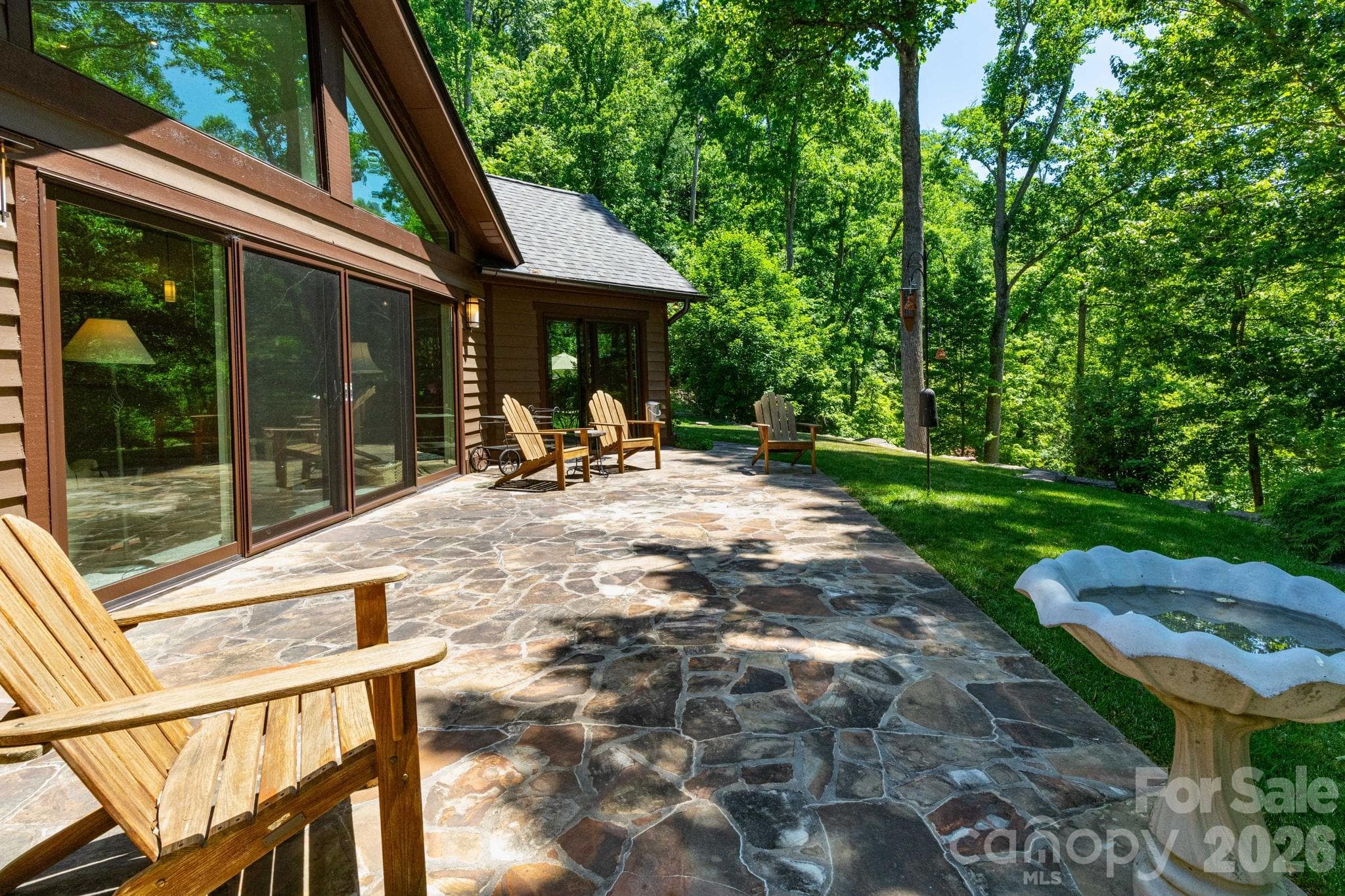 Thoughtfully designed outdoor living spaces invite relaxation and connection with nature. The stone patio, dramatic windows, and warm wood tones give the home a timeless mountain-modern feel. - 29 Gardner Drive, Asheville