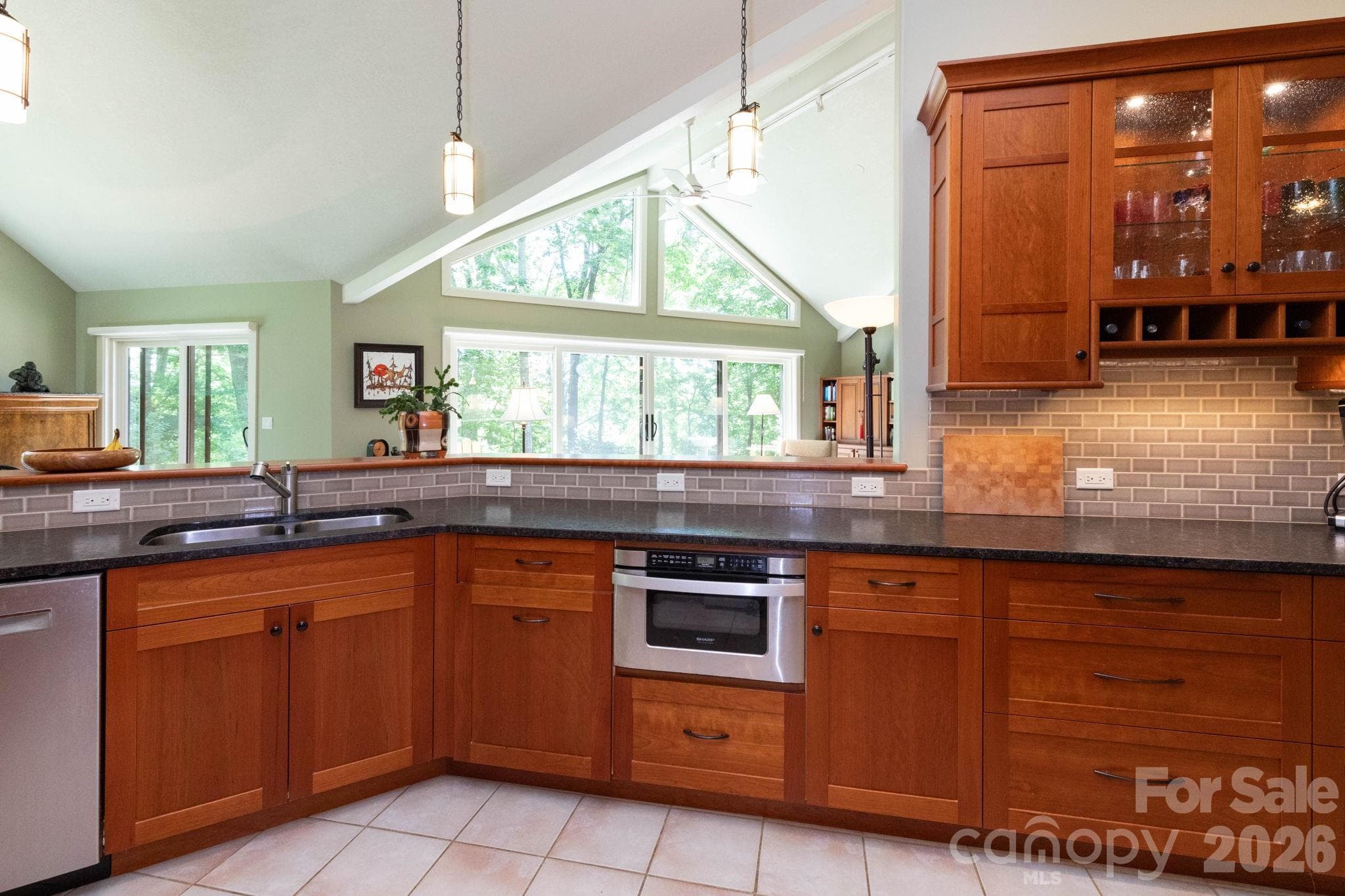Well-appointed kitchen featuring custom cabinetry, sleek countertops, tile backsplash, and an open design overlooking the main living spaces and surrounding nature views. - 29 Gardner Drive, Asheville