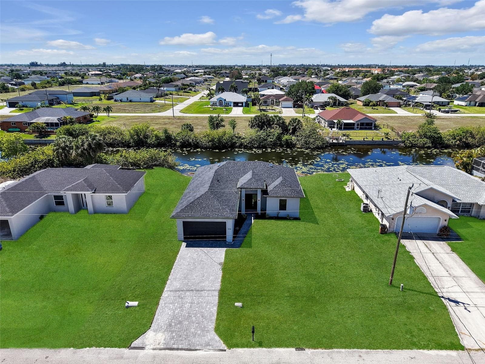 Newly constructed residence featuring a dark shingle roof, paver driveway, and a spacious lawn the color of the grass has been virtually enhanced - 1310 NW 11TH TER, CAPE CORAL