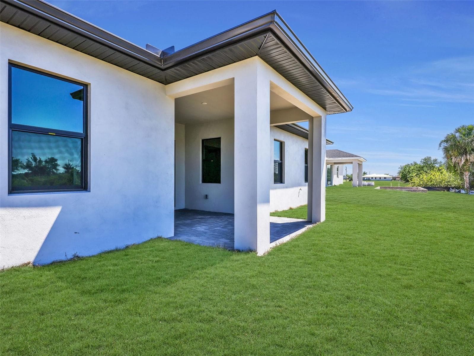 Newly constructed residence featuring a dark shingle roof, paver driveway, and a spacious lawn the color of the grass has been virtually enhanced - 1310 NW 11TH TER, CAPE CORAL