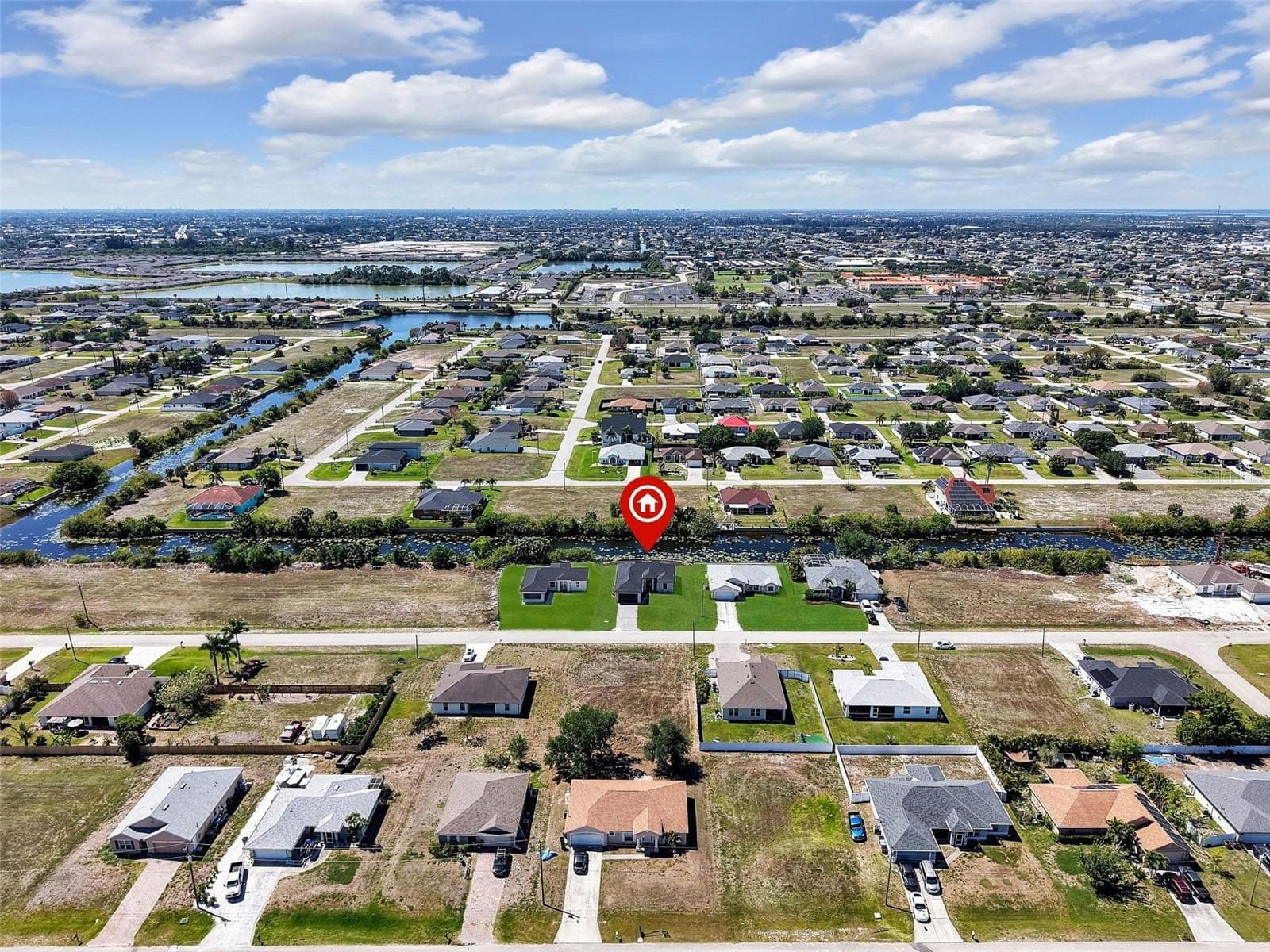 Aerial perspective showcasing a residential neighborhood with numerous single-story homes, many featuring paved driveways and green lawns the color of the grass has been virtually enhanced - 1310 NW 11TH TER, CAPE CORAL