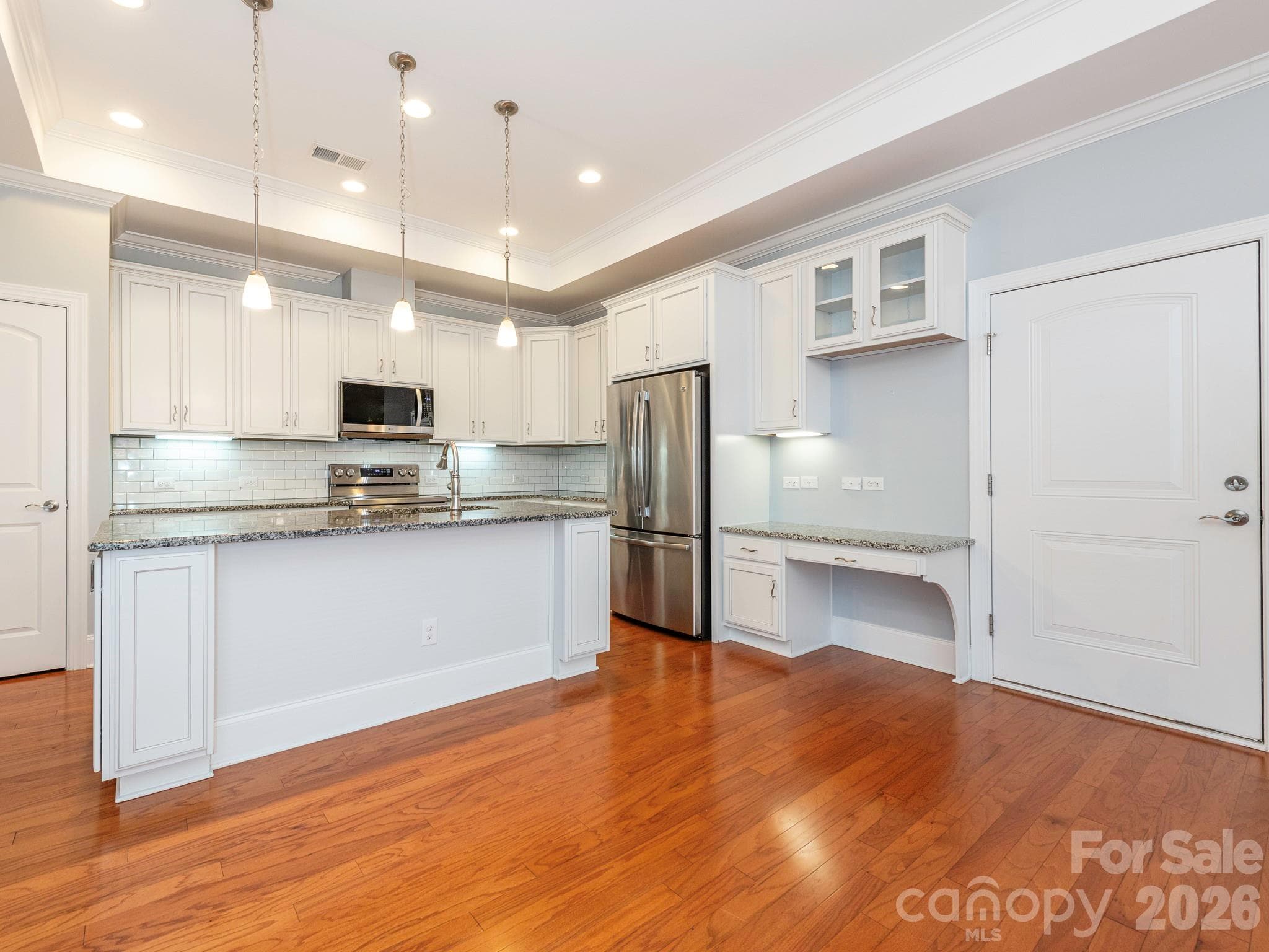 Kitchen has a large island with pendant lighting, convenient pantry (door on the left), and desk area, as well as easy access to the garage (door on the right). - 4534 Ideal Way, Harrisburg