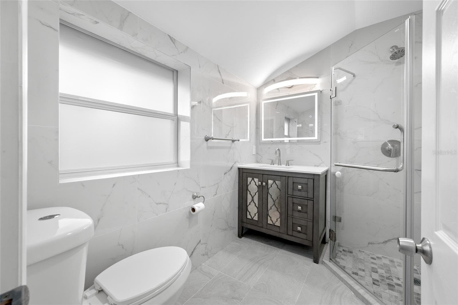 Primary Bedroom suite with walk-in closet, with built in shevles, that opens through to private en-suite updated bathroom with marble tile and glass shower. - 5044 BETTY ST N, ST PETERSBURG