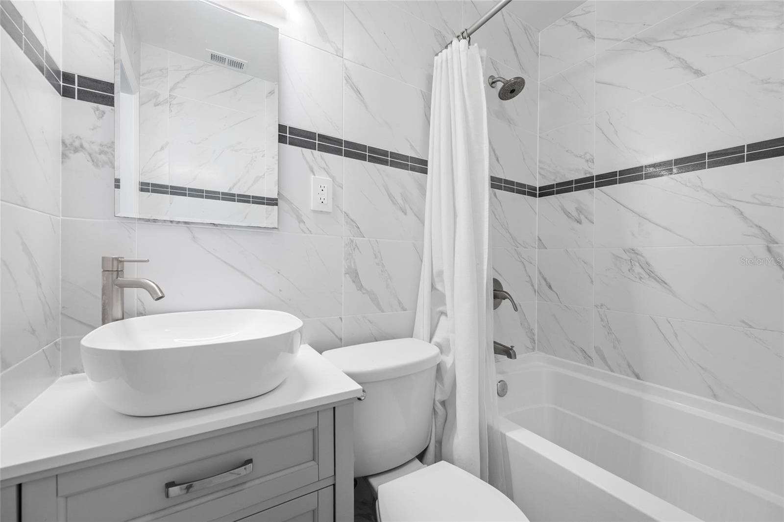 Bathroom 2 features an upgraded vanity, marble tiles, and a bathtub with shower. - 5044 BETTY ST N, ST PETERSBURG