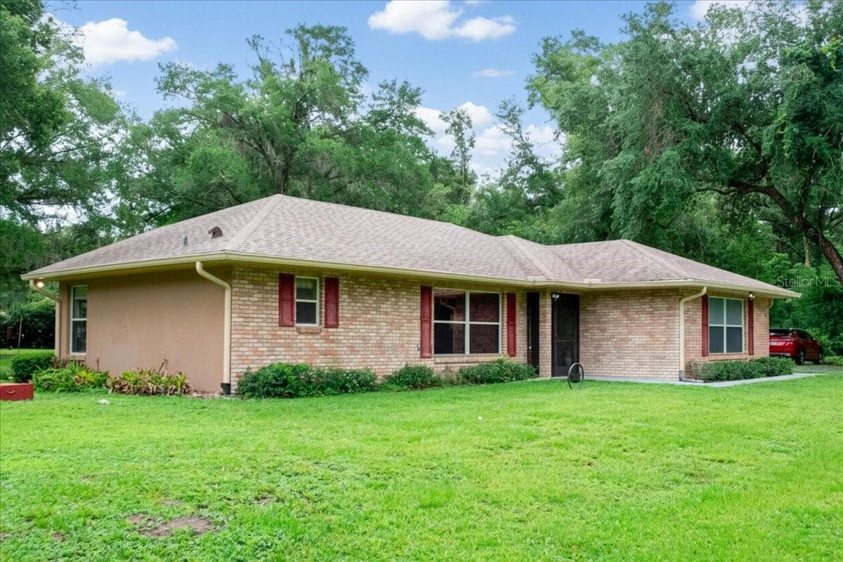 Angled exterior view showcasing the brick construction and covered front porch. - 267 N ORANGE AVE, LAKE HELEN