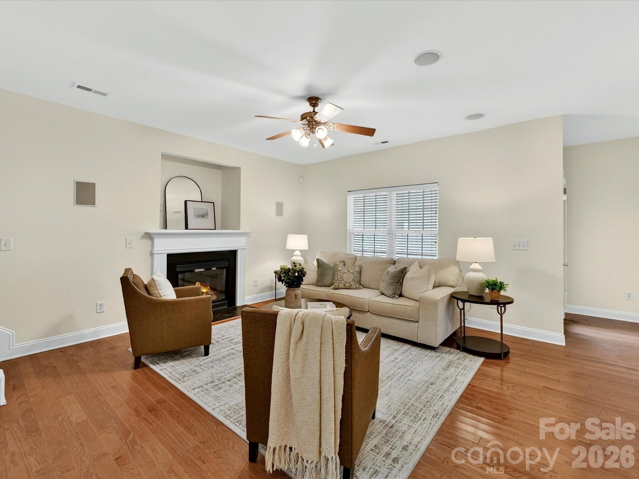 Spacious great room features wood flooring, a cozy fireplace with classic mantel, and an open-concept layout designed for comfortable everyday living and effortless entertaining. - Cornelius
