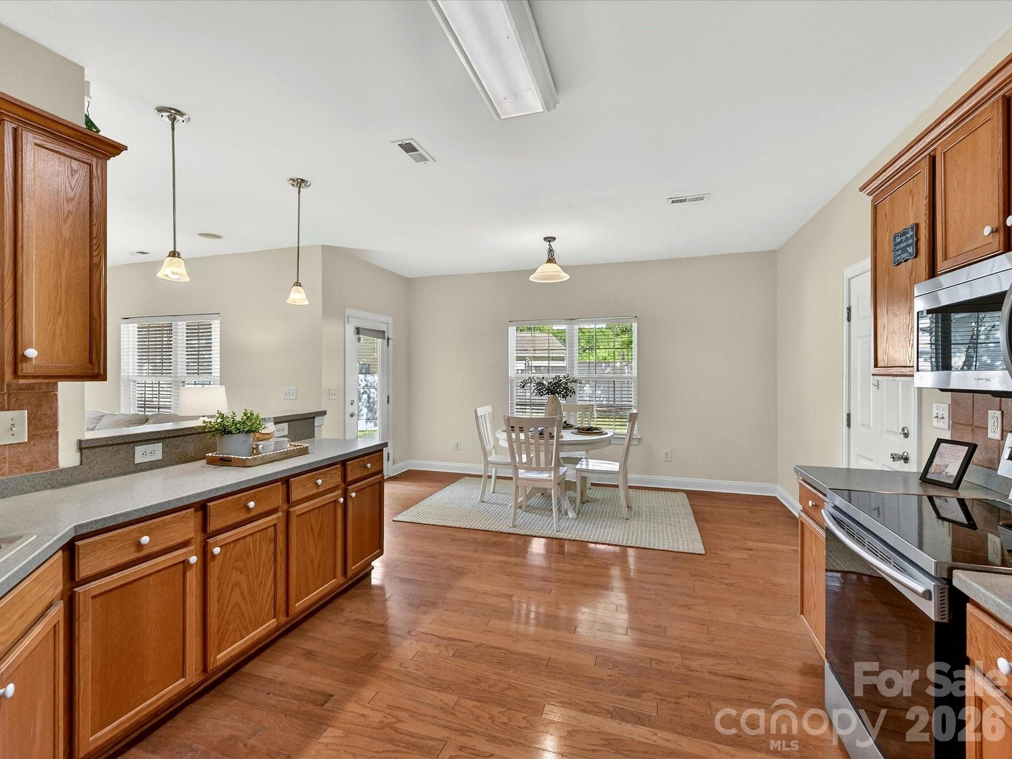 Spacious kitchen offers abundant cabinetry, expansive solid surface counters, stainless steel appliances, hardwood flooring, and a seamless connection to the breakfast area and main living spaces. - Cornelius