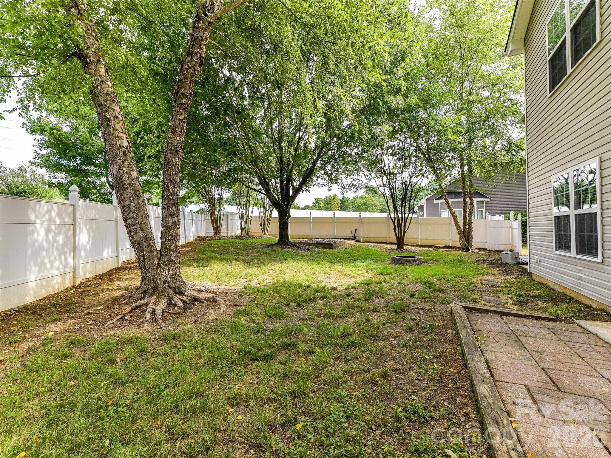 Private fenced backyard features mature shade trees, a patio area for outdoor entertaining, and a dedicated fire pit gathering space, creating the perfect setting for relaxation and recreation. - Cornelius