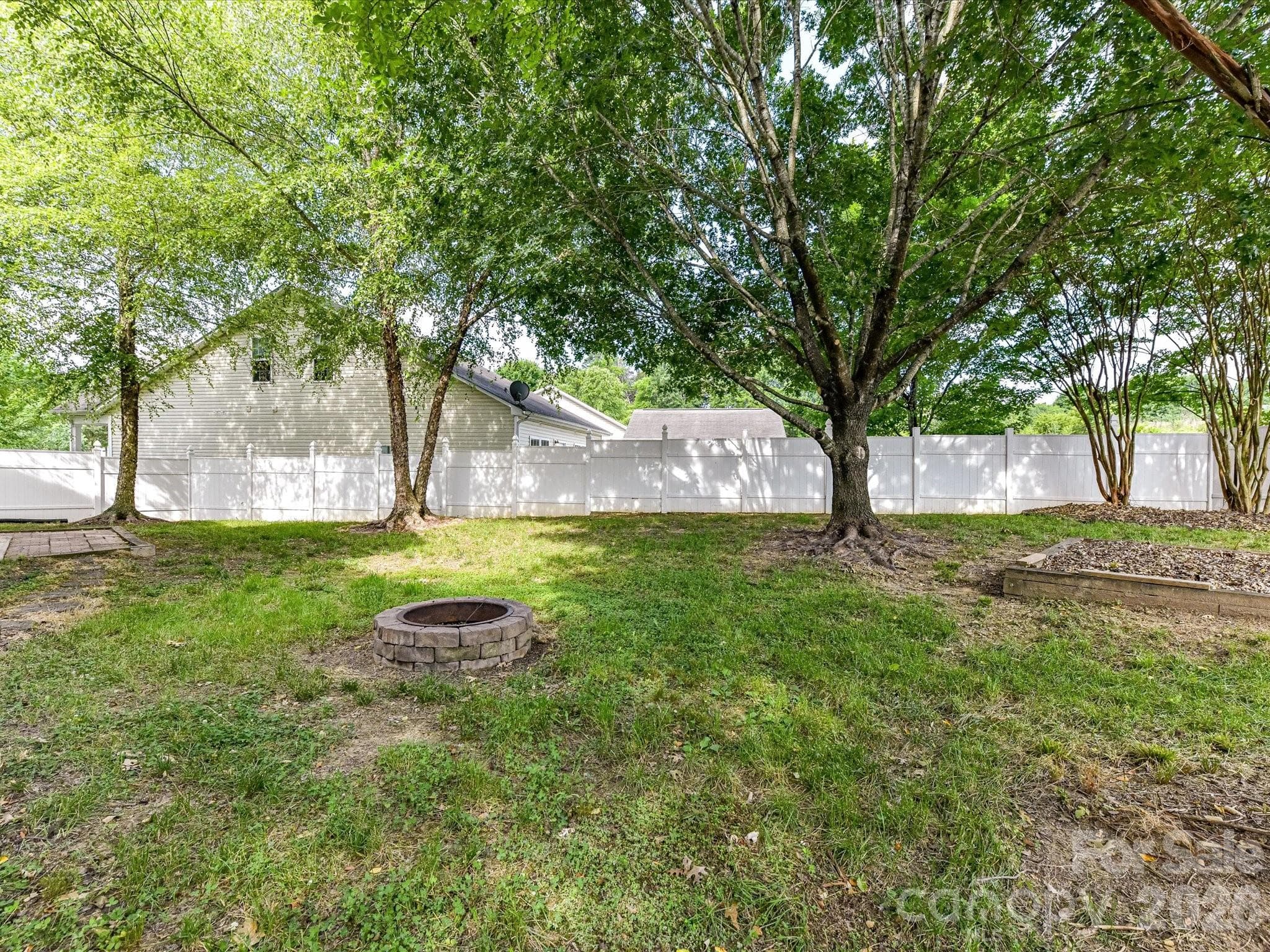 Private fenced backyard features mature shade trees, a patio area for outdoor entertaining, and a dedicated fire pit gathering space, creating the perfect setting for relaxation and recreation. - Cornelius