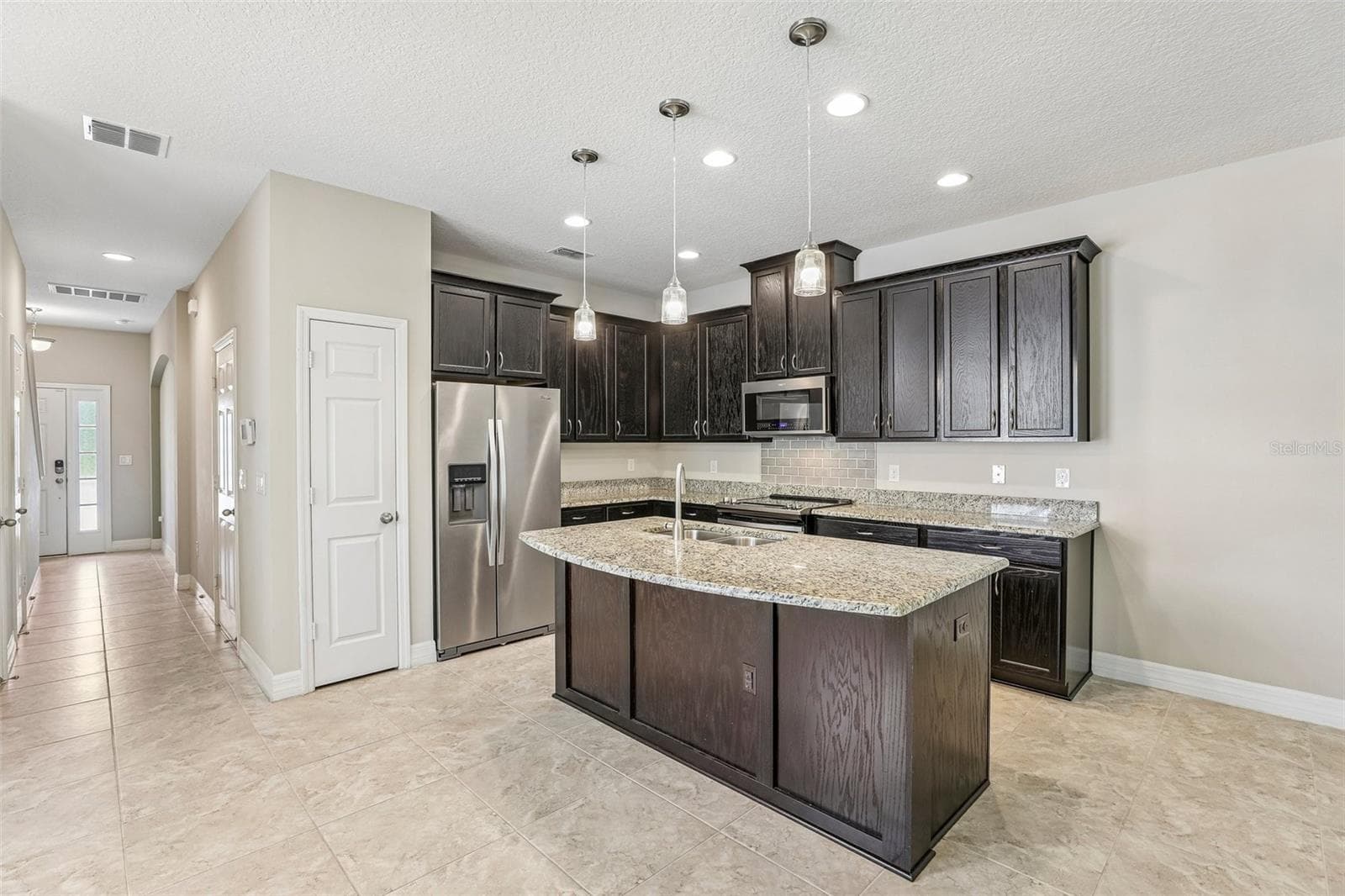 The OPEN CONCEPT main floor is designed for everyday living and easy entertaining, featuring a modern kitchen with rich cabinetry, GRANITE COUNTERTOPS, pantry storage, UPGRADED STAINLESS STEEL APPLIANCES, a large ISLAND with bar seating, pendant lighting, and recessed lighting. - 198 MITCHELL CREEK WAY, OVIEDO