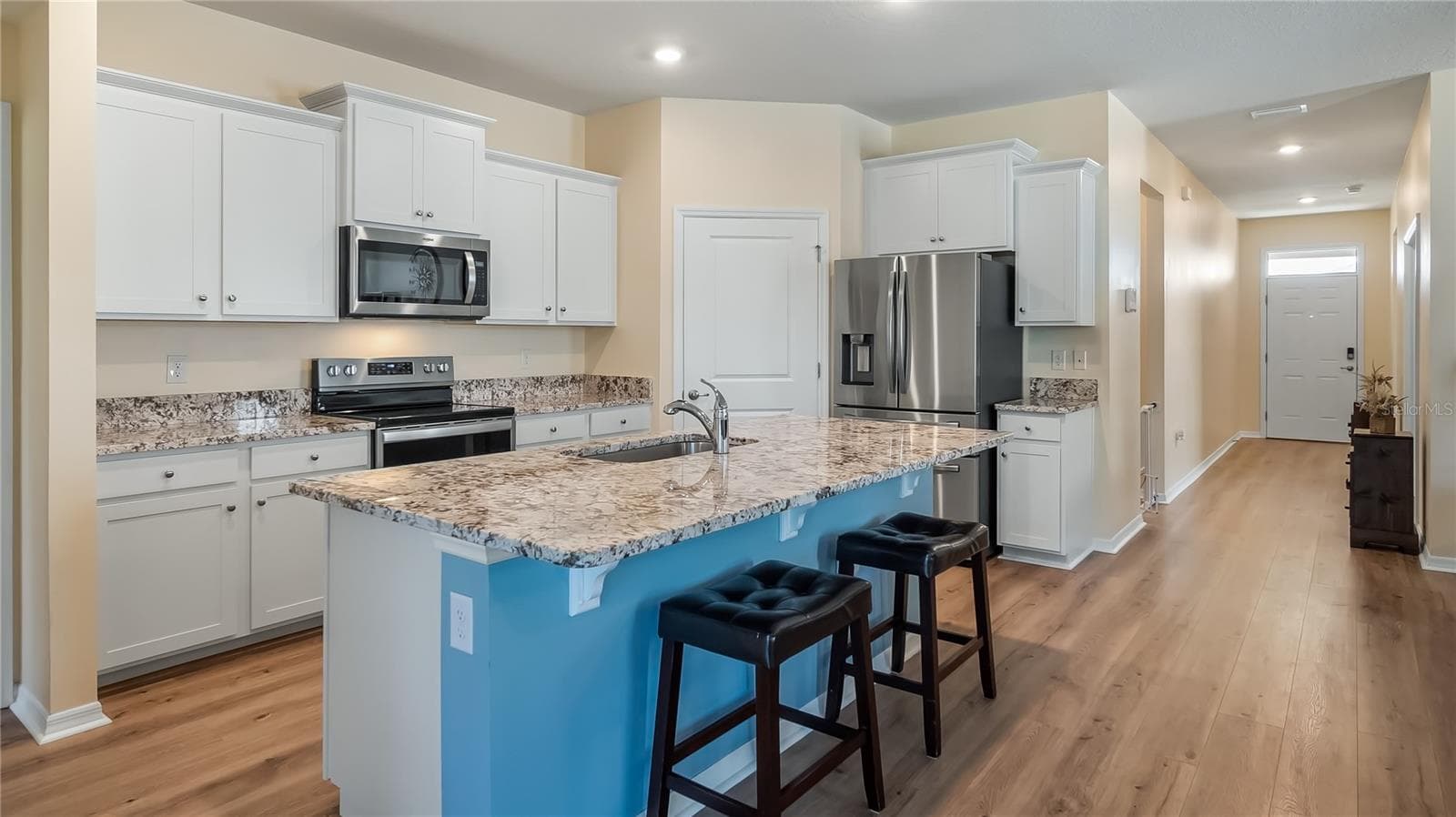 The kitchen is equipped with stainless steel appliances, granite countertops, and a breakfast bar overlooking the living room and dining room. - 8033 PENROSE PL, WILDWOOD