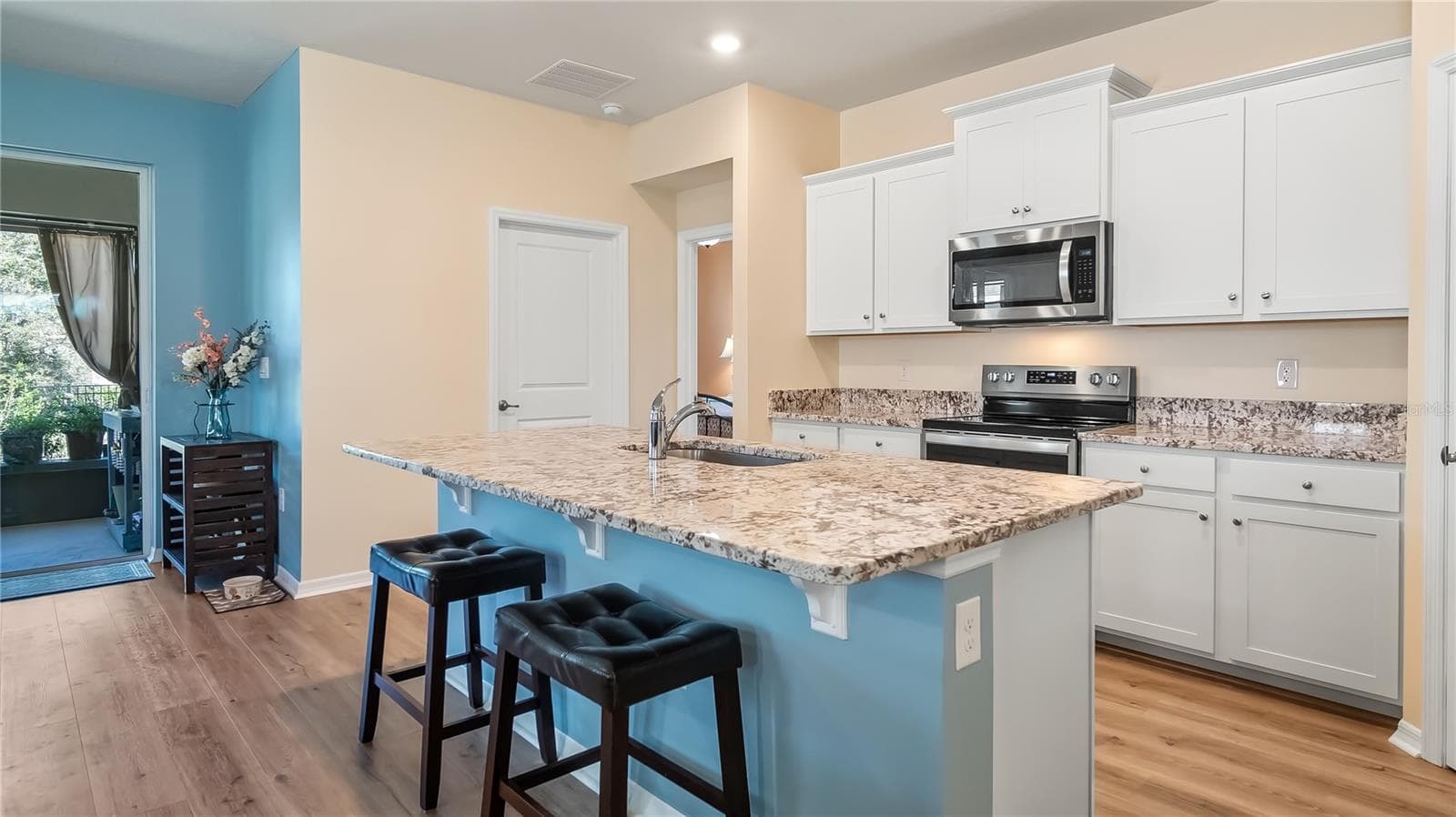 The kitchen is equipped with stainless steel appliances, granite countertops, and a breakfast bar overlooking the living room and dining room. - 8033 PENROSE PL, WILDWOOD