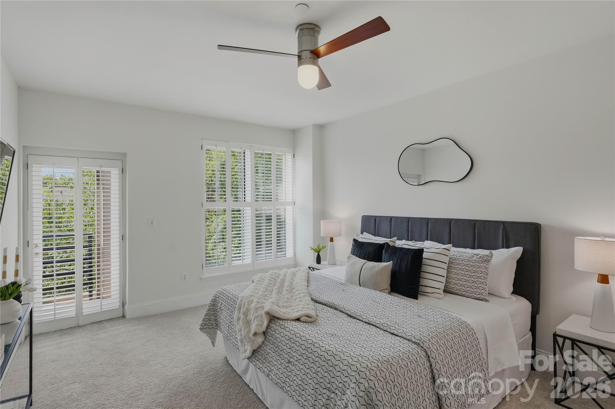 Wake up to greenery and natural light in the spacious primary suite featuring French doors to a private balcony, plantation shutters, plush carpet, and a ceiling fan for year-round comfort. - Charlotte