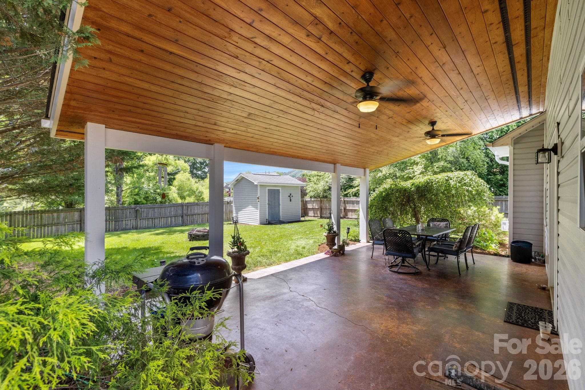 Expansive covered patio with wood-paneled ceiling and ceiling fans, creating an ideal outdoor living and entertaining space. - Fletcher
